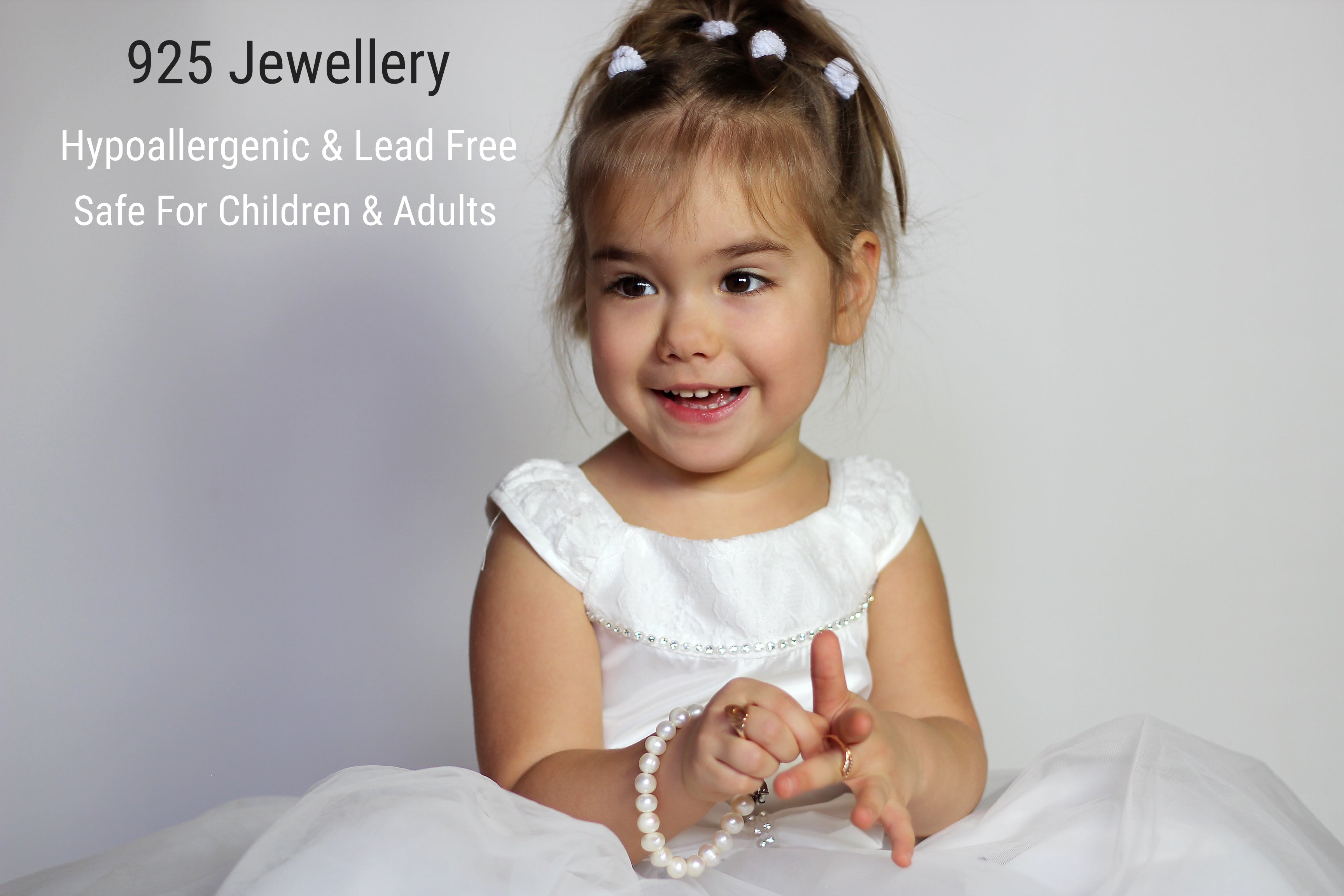 Smiling young girl in a white dress holding a pearl bracelet featuring the best hypoallergenic jewellery for children