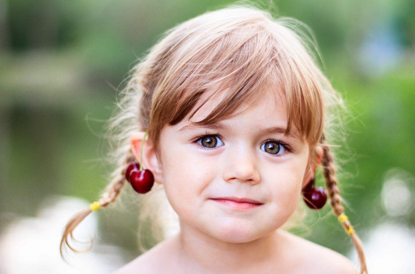 Little girl with light blonde hair in pigtails wearing stylish sterling silver earrings for babies with red cherry design outdoors