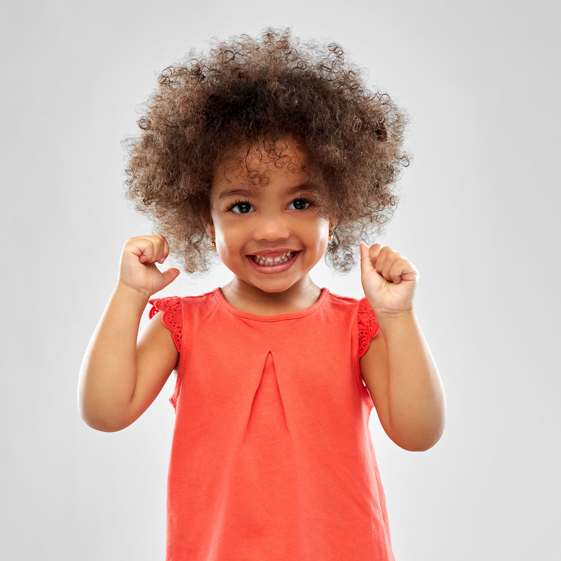 Smiling young child raising fists with curly hair wearing red top jewellery safety tips for children