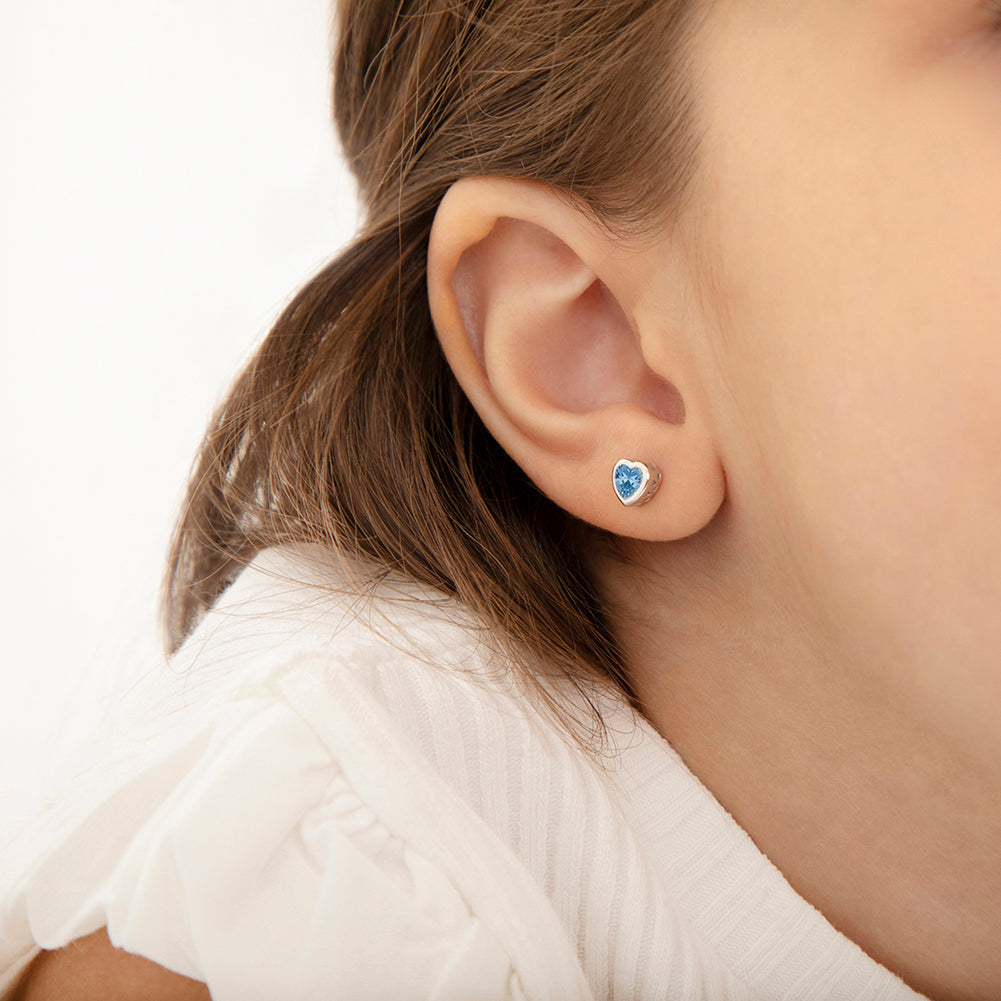 Close-up of a child's ear wearing silver heart-shaped best screw back earrings for children with bright blue stones