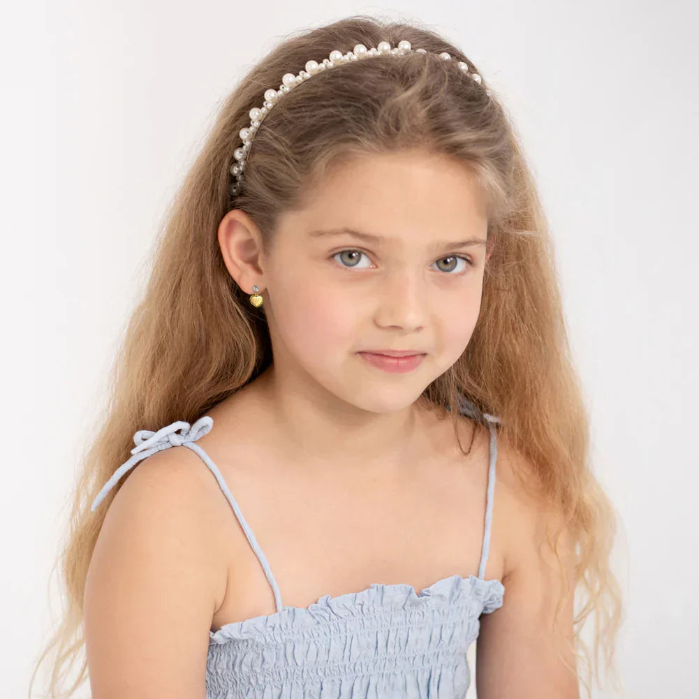 Young girl with long blonde hair wearing delicate gold earrings for young girls and a light blue dress with a pearl headband