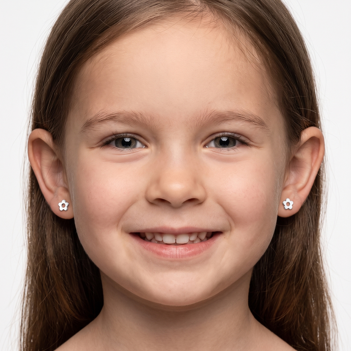 A close-up portrait of a young girl with brown hair wearing small silver flower-shaped stud earrings