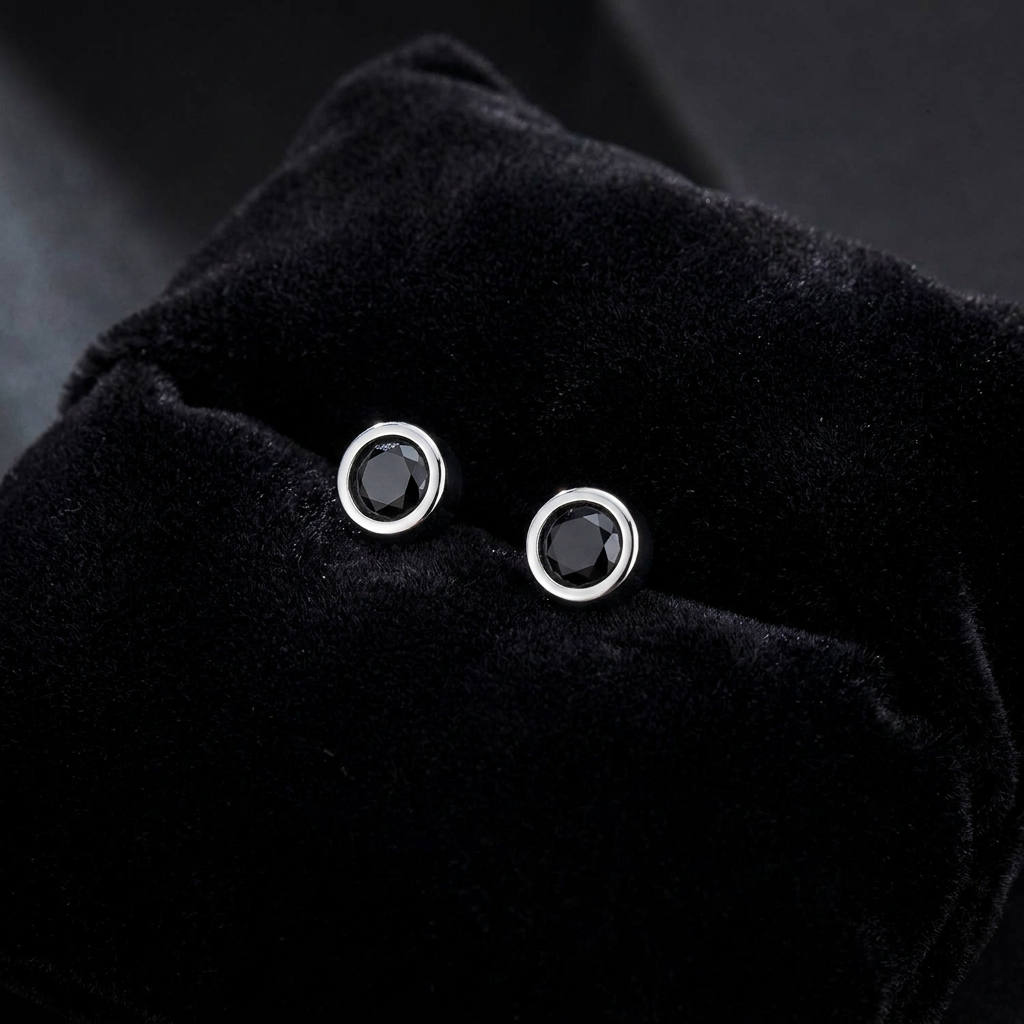 A pair of silver stud earrings with round black gemstones, displayed on a black velvet jewelry pouch.