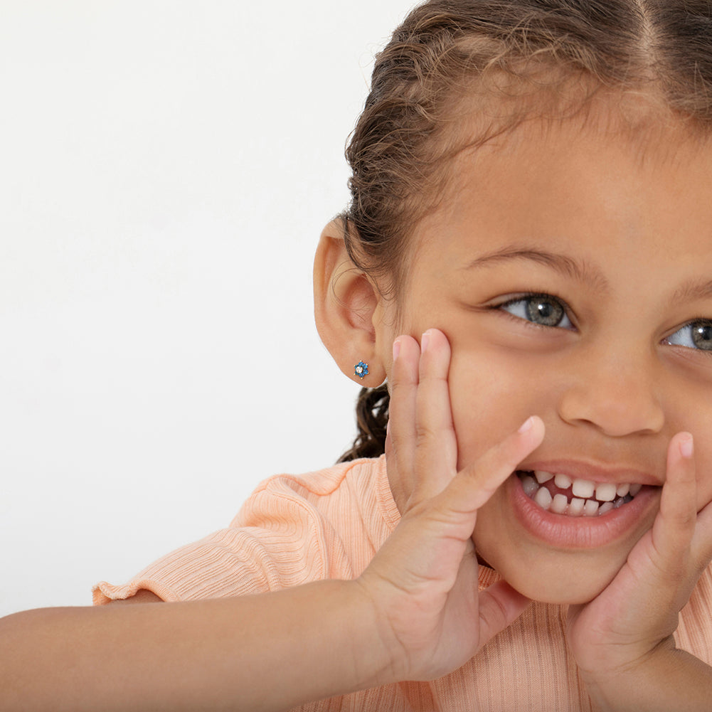 Smiling child wearing 14k gold kids flower earrings from In Season Jewellery in blue design
