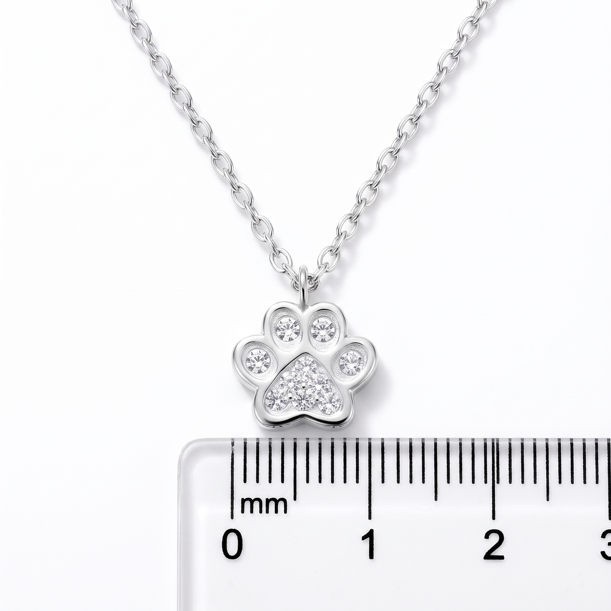 A silver-tone paw print pendant necklace on a matching chain, shown above a ruler for scale
