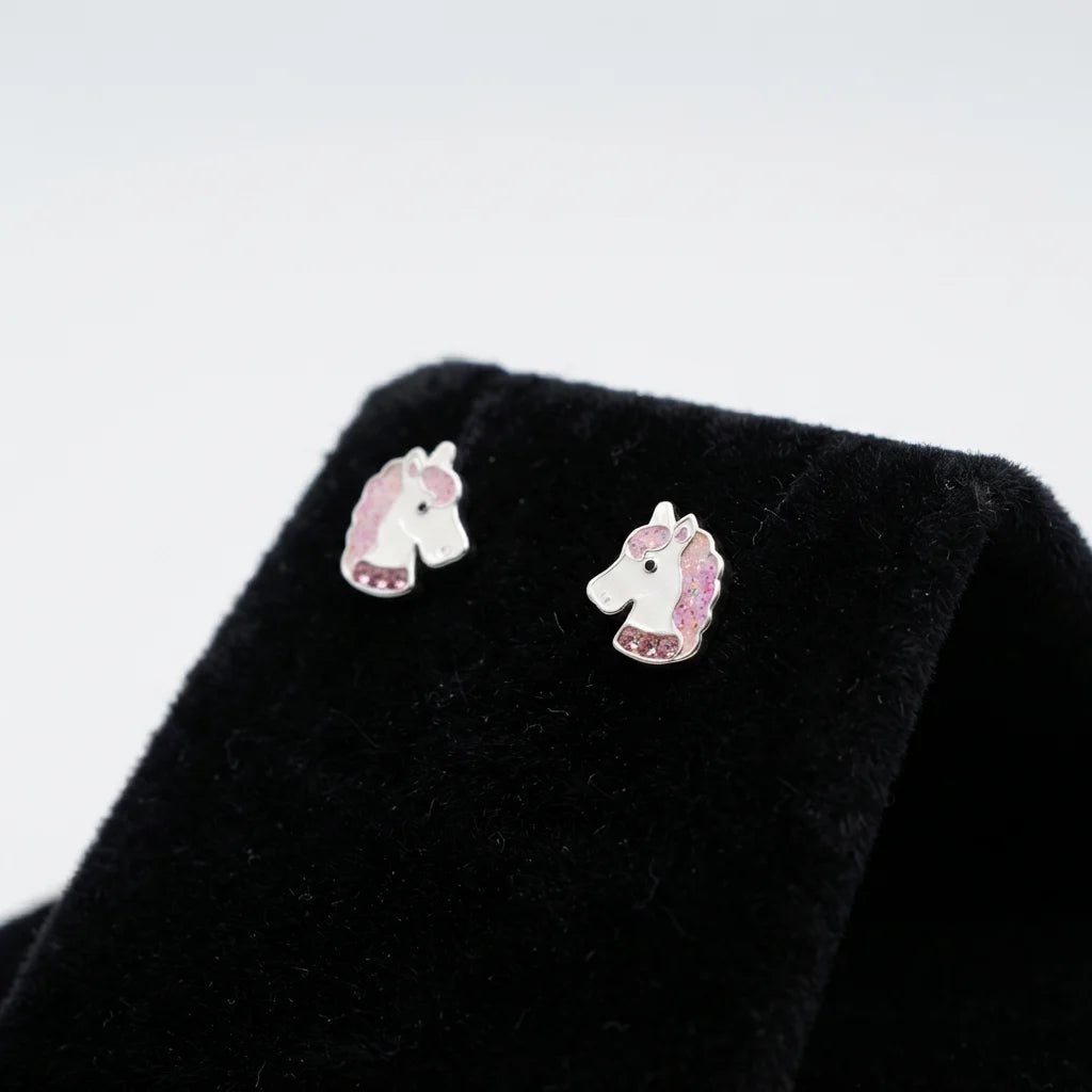 A pair of silver unicorn stud earrings with pink and white enamel detailing, displayed on a black velvet jewelry stand against a light gray background.