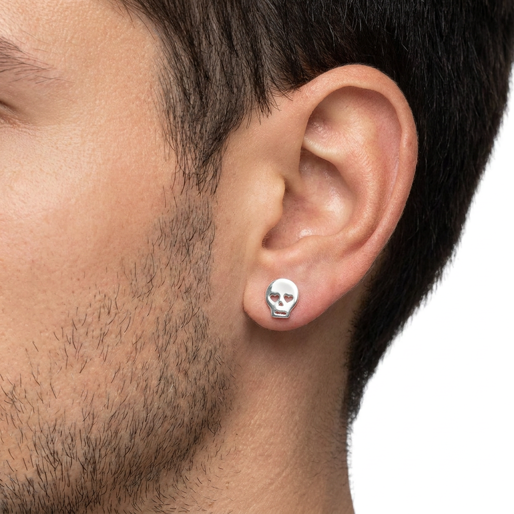 A close-up of a man's ear wearing a small silver skull stud earring against a plain white background.