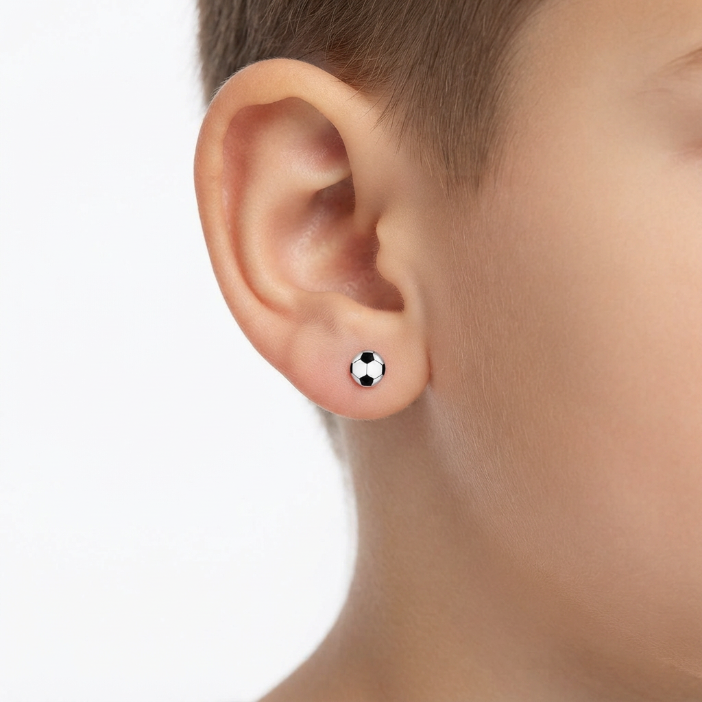 A close-up of a child's ear wearing a small black and white soccer ball stud earring against a clean white background.