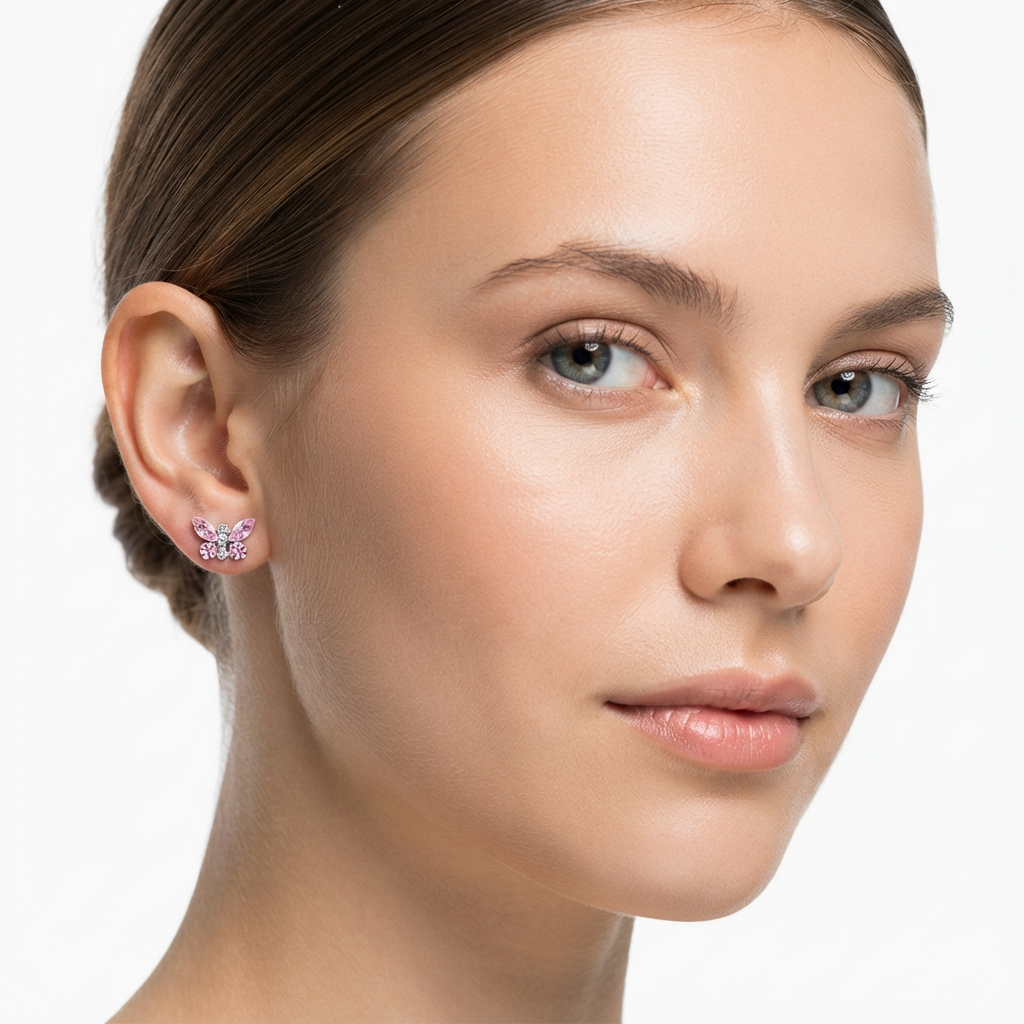 A close-up of a woman's ear wearing a small butterfly-shaped stud earring with sparkling clear stones and a pink center, against a clean white background.