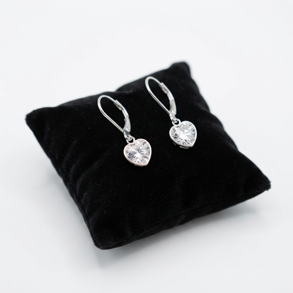 A pair of silver leverback earrings with heart-shaped clear rhinestones, displayed on a black velvet cushion against a white background.