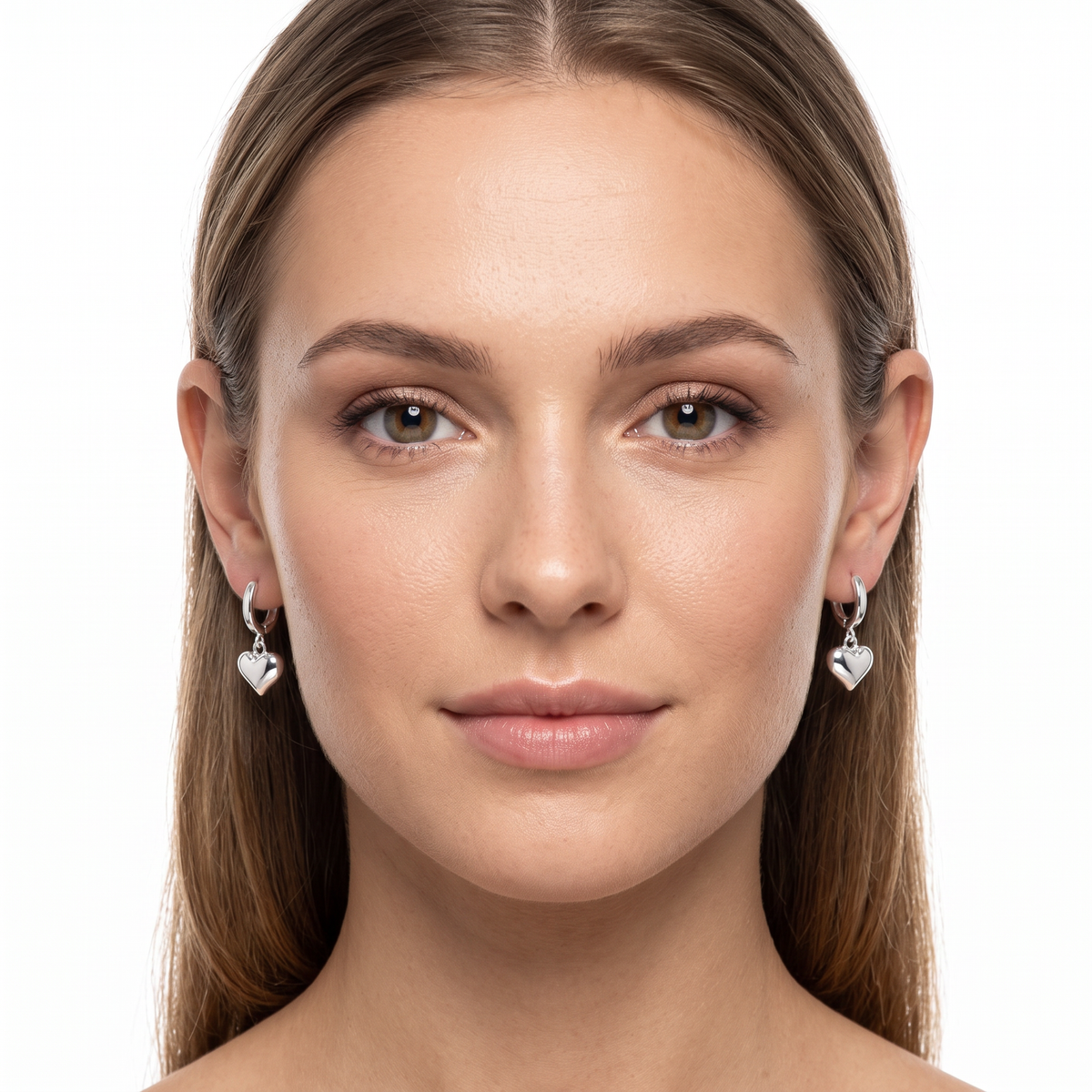 A close-up portrait of a woman wearing small silver heart-shaped dangle earrings