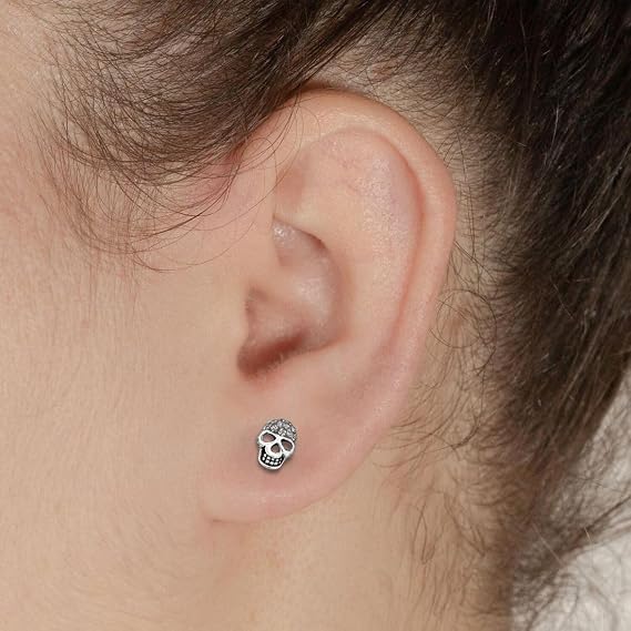 A close-up of a person's ear wearing a small silver skull stud earring.