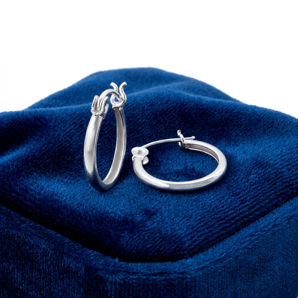 A pair of polished silver hoop earrings with unique textured and floral details, displayed on a textured dark blue velvet surface