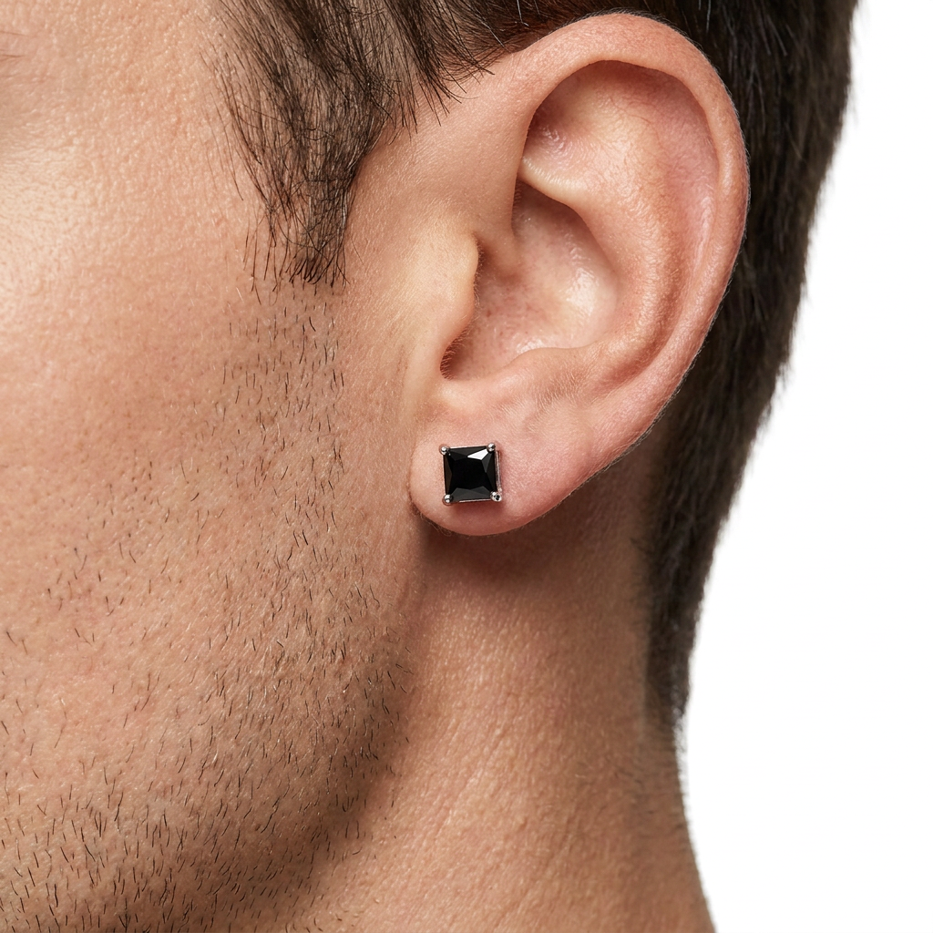 A close-up of a man's ear wearing a small square stud earring with a black center and a silver-toned bezel setting.