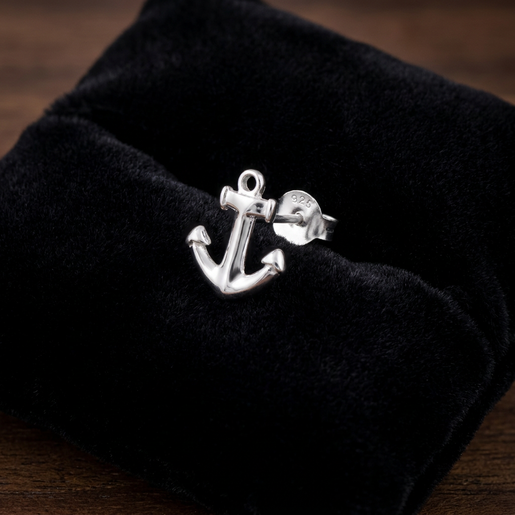 A silver anchor ring displayed on a black velvet jewelry box, set against a dark wooden background.