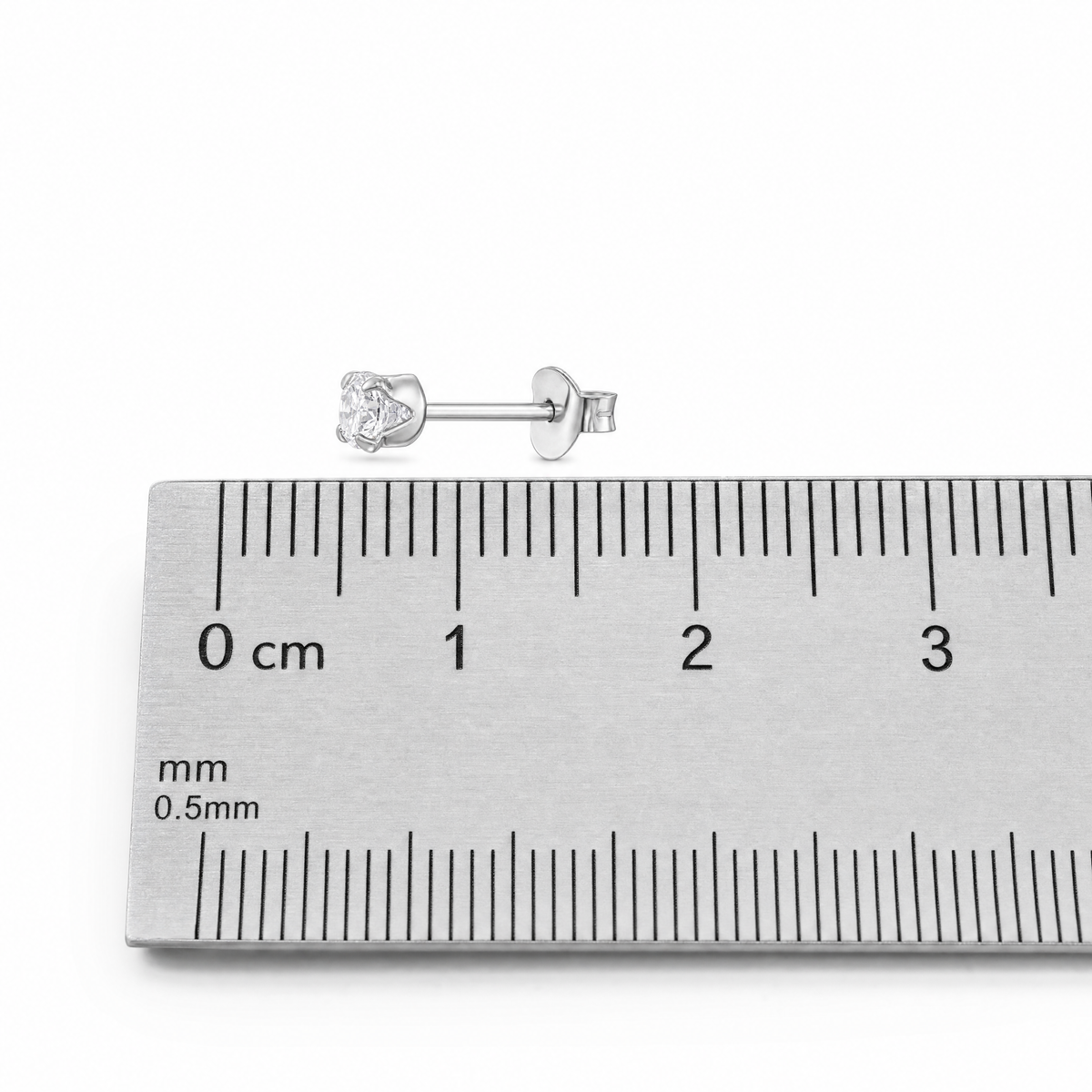A single silver stud earring with a clear gemstone, positioned above a metal ruler showing centimeter and millimeter markings for scale.