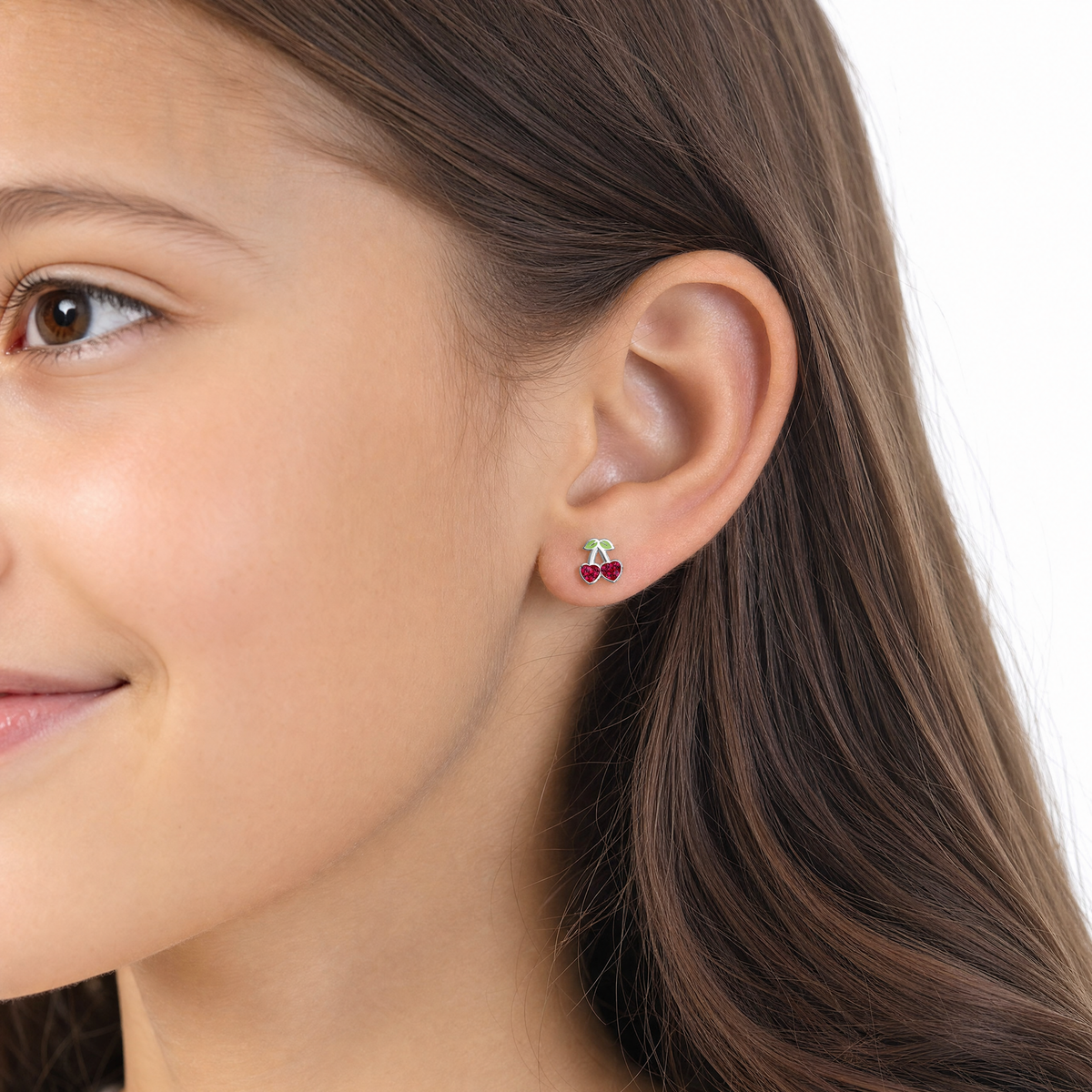 A close-up of a young girl ear wearing a small cherry stud earring with red gemstones and a green leaf detail.