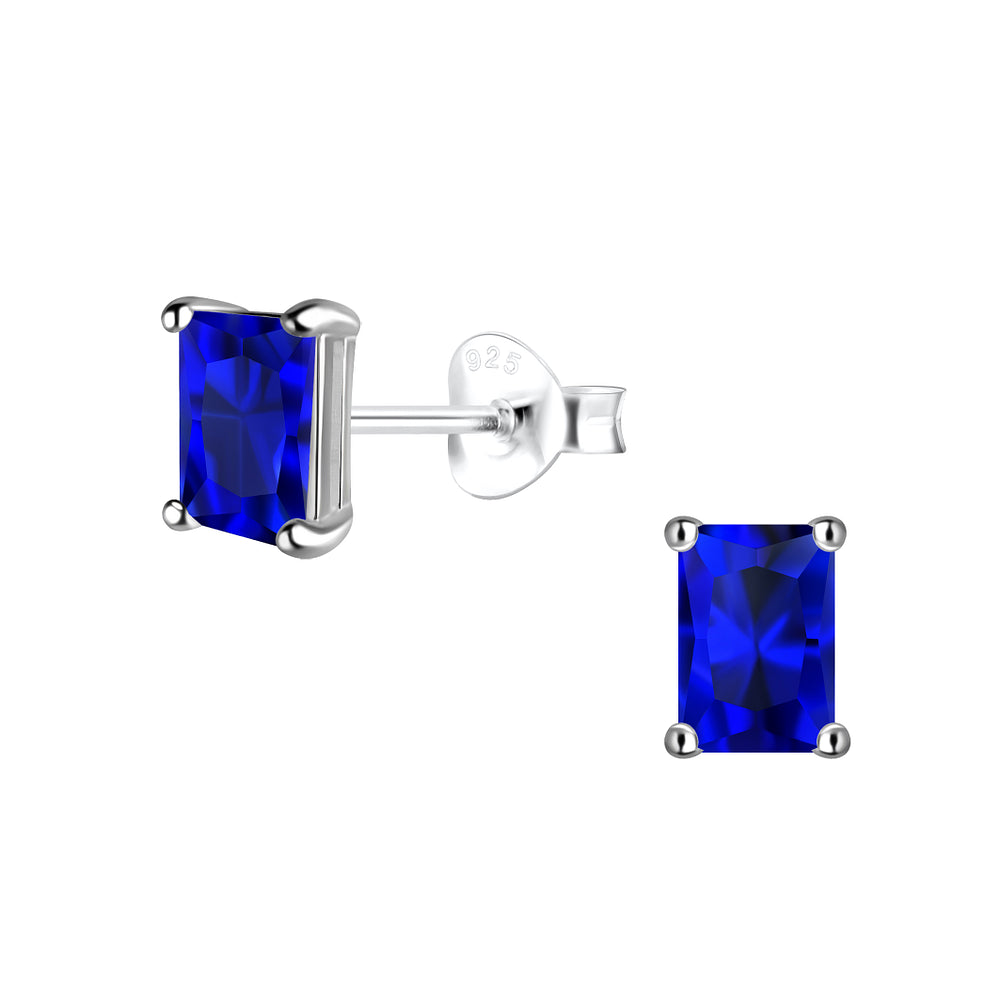 A pair of rectangular blue gemstone stud earrings in silver prong settings, with one earring shown from the front and the other from the side showing the post and butterfly back. The metal is sterling silver, indicated by a '925' stamp on the backing.