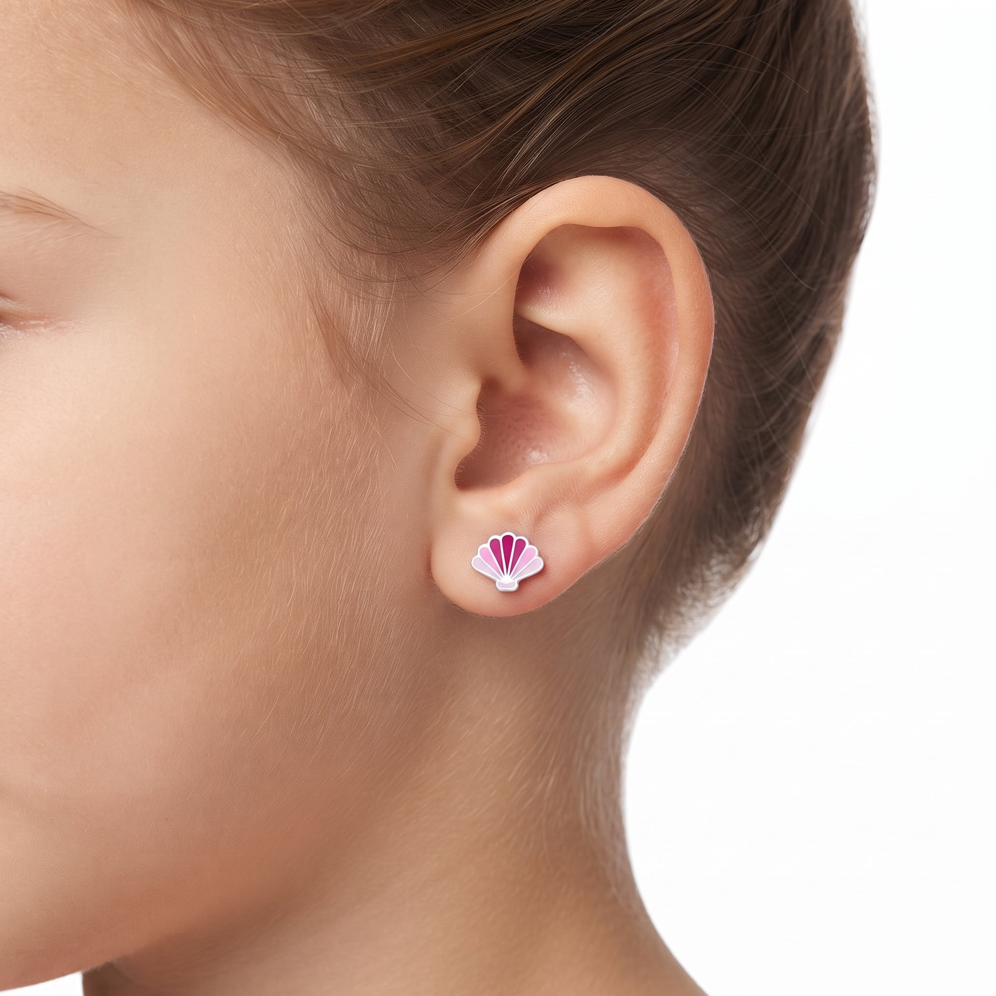 A close-up of a child's ear wearing a small seashell stud earring with pink and white enamel details, set against a clean white background.