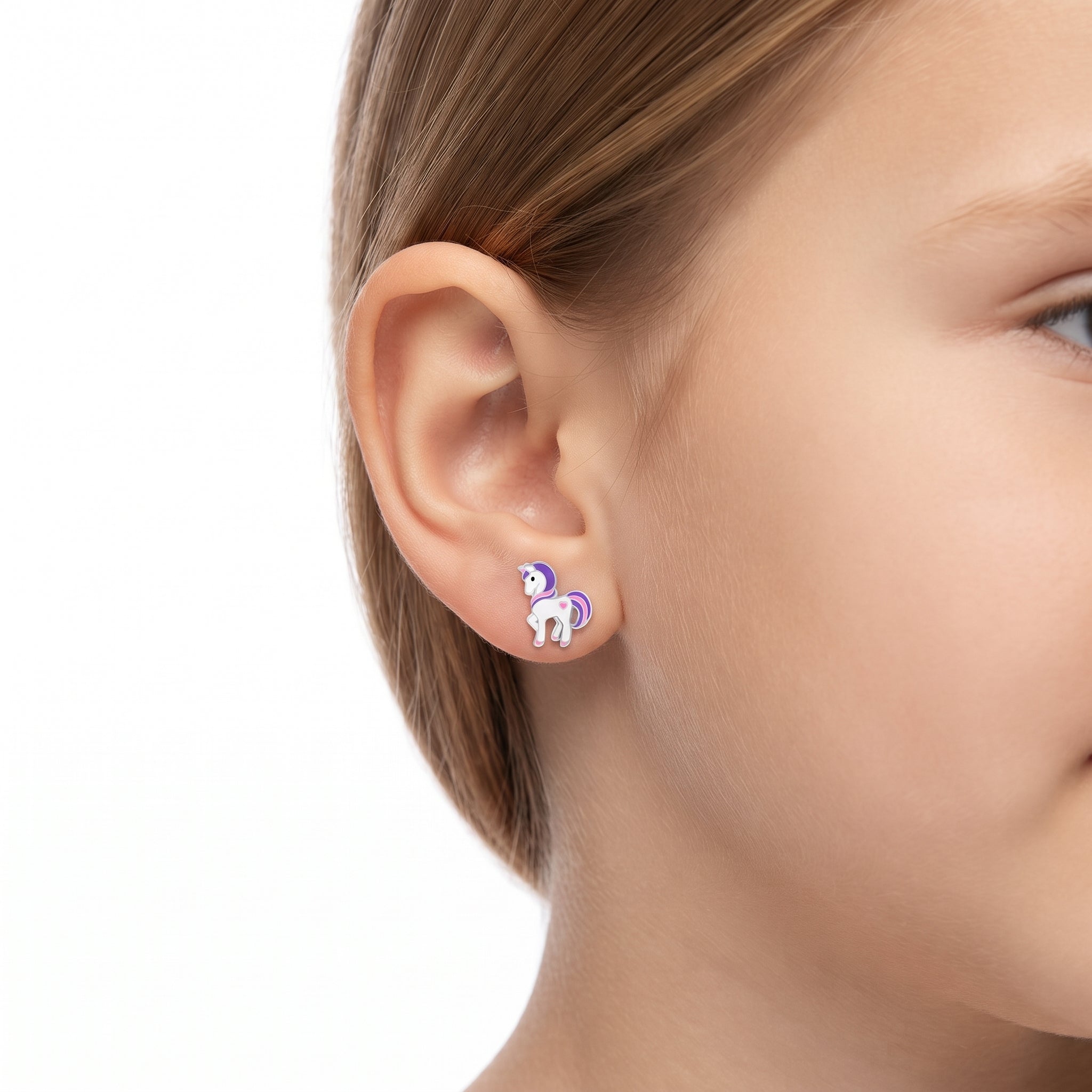 A close-up of a child's ear wearing a small unicorn stud earring. The earring features a white unicorn with a purple mane and tail, set against a plain white background.
