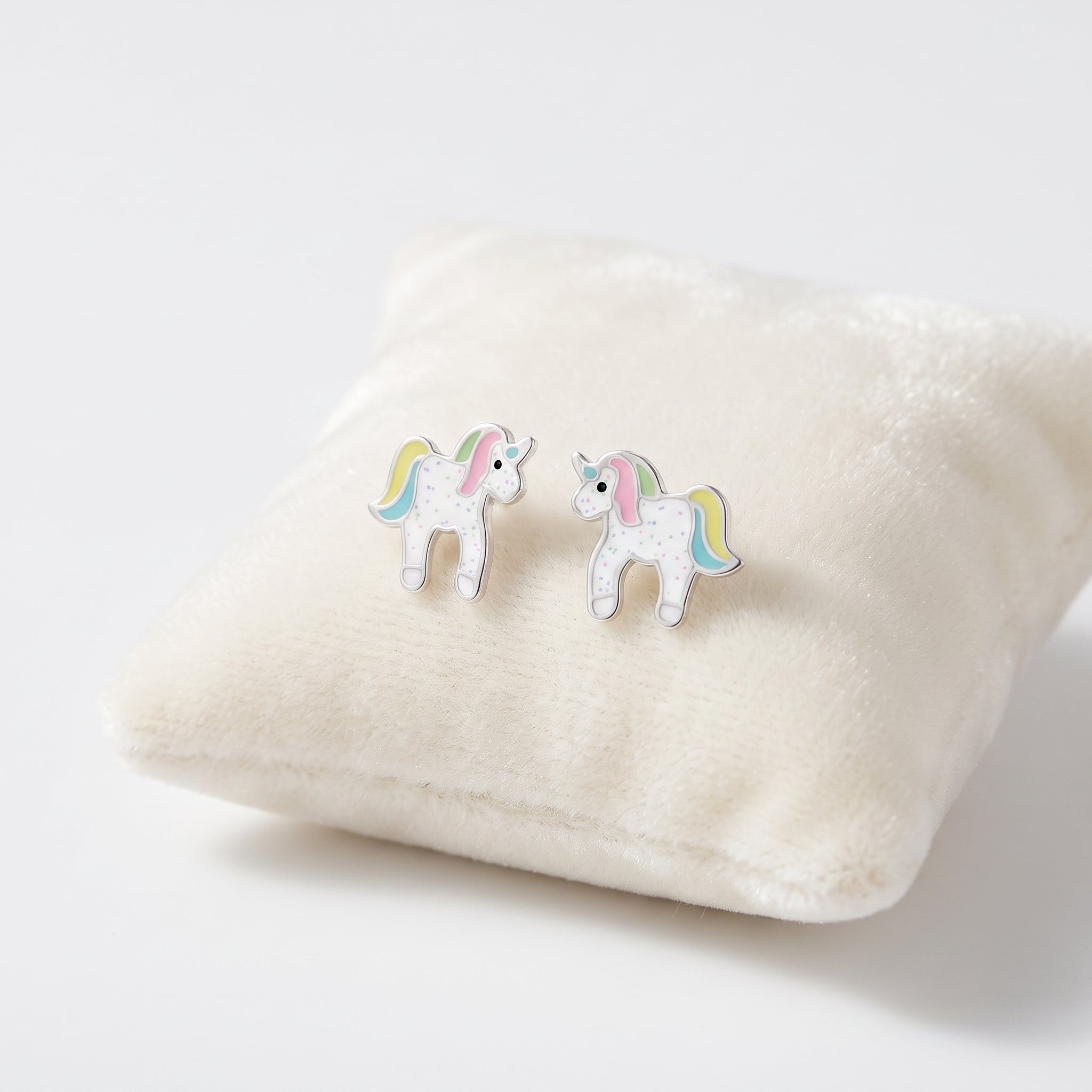 A pair of small unicorn stud earrings with white bodies, pastel rainbow manes and tails