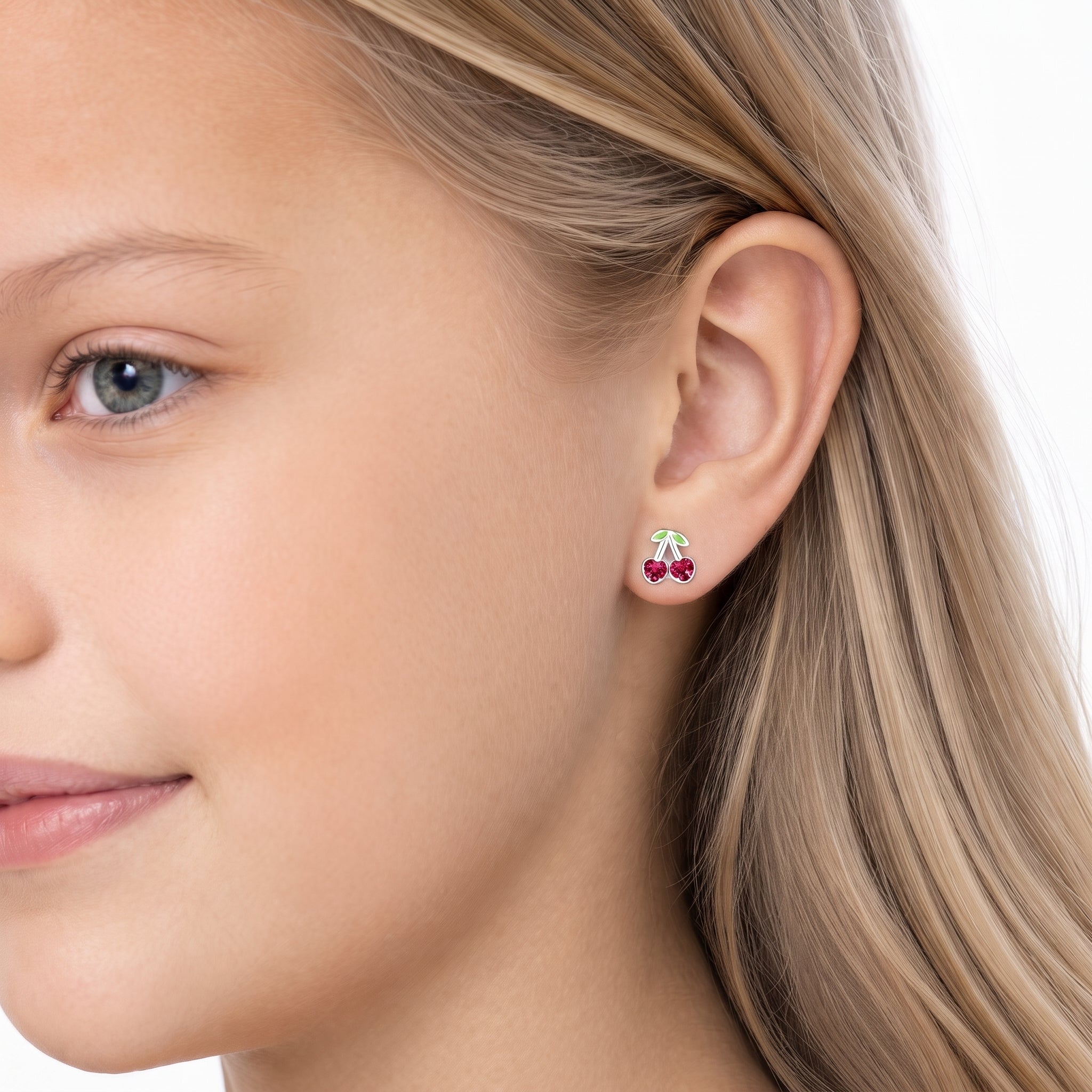 A close-up of a young girl's face and ear wearing a small cherry stud earring.