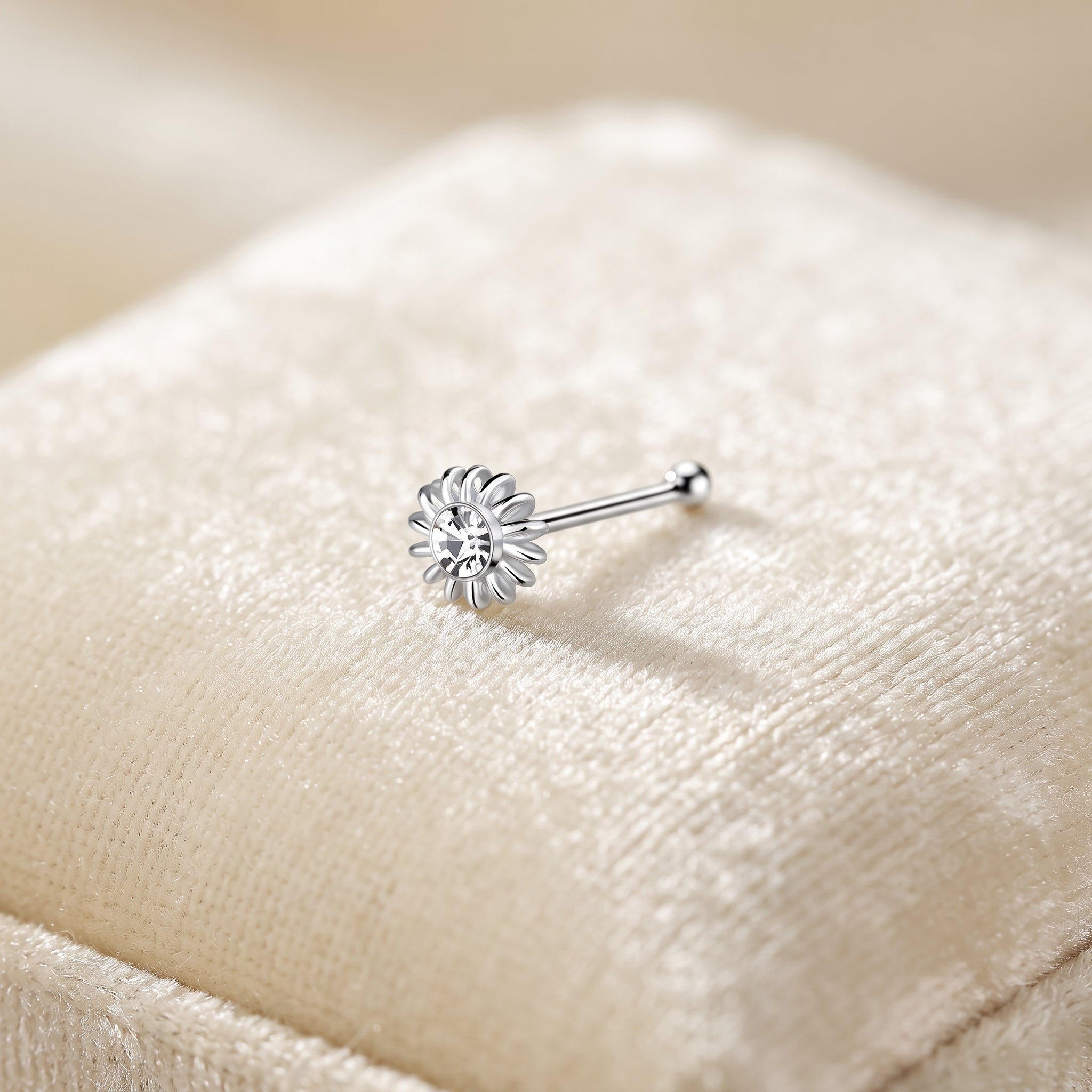 A silver flower-shaped stud earring with a clear central gemstone, resting on a soft beige textured fabric surface.