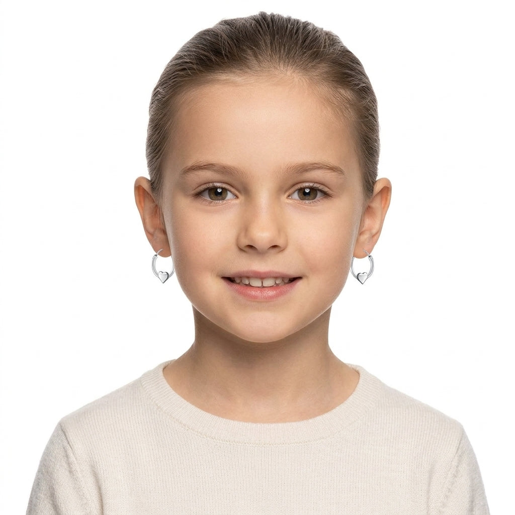 Young girl wearing silver girls heart charm hoop earrings by Melchior Jewellery with delicate heart-shaped charms