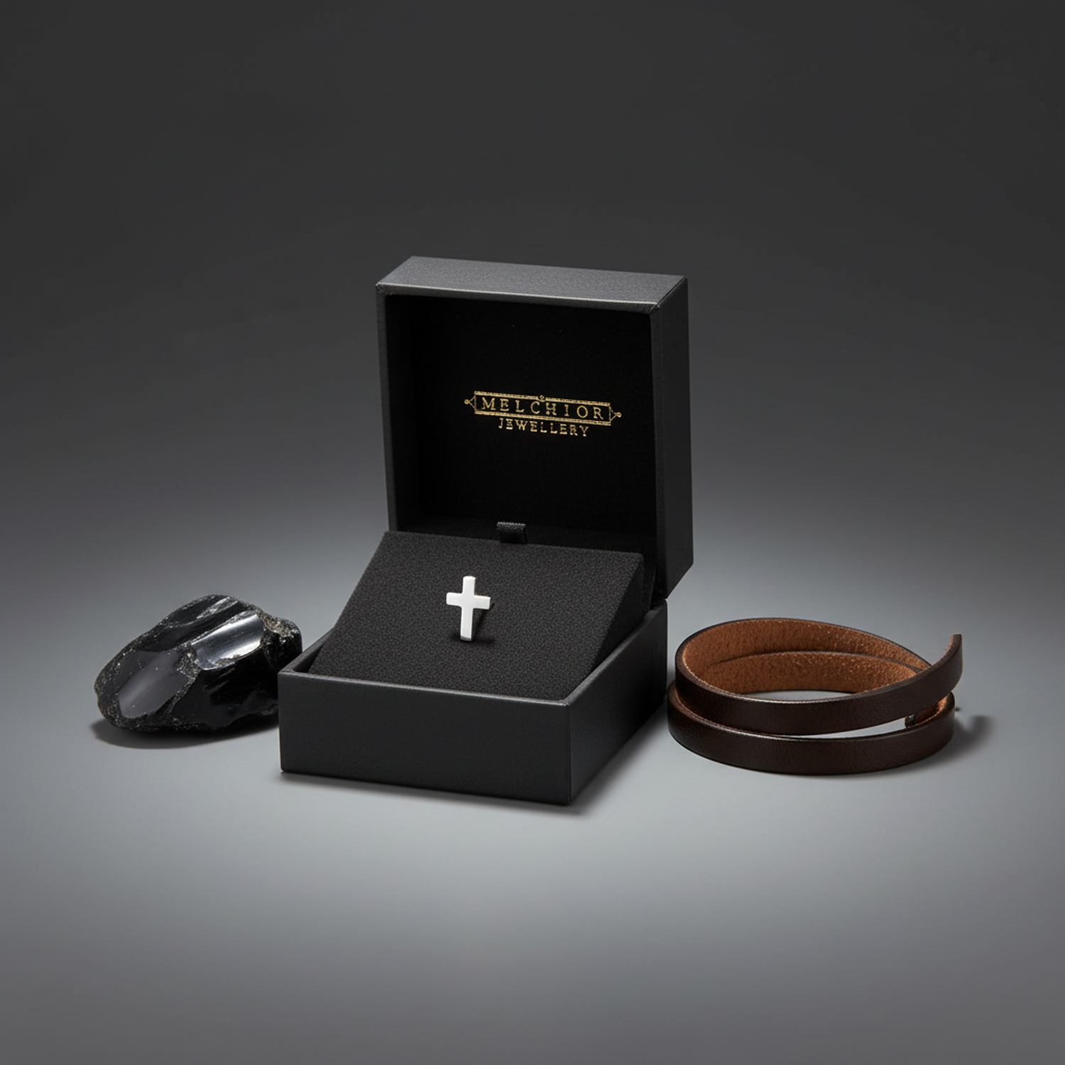 Sterling silver mens cross stud earring displayed in Melchior Jewellery black box with leather bracelet and black stone