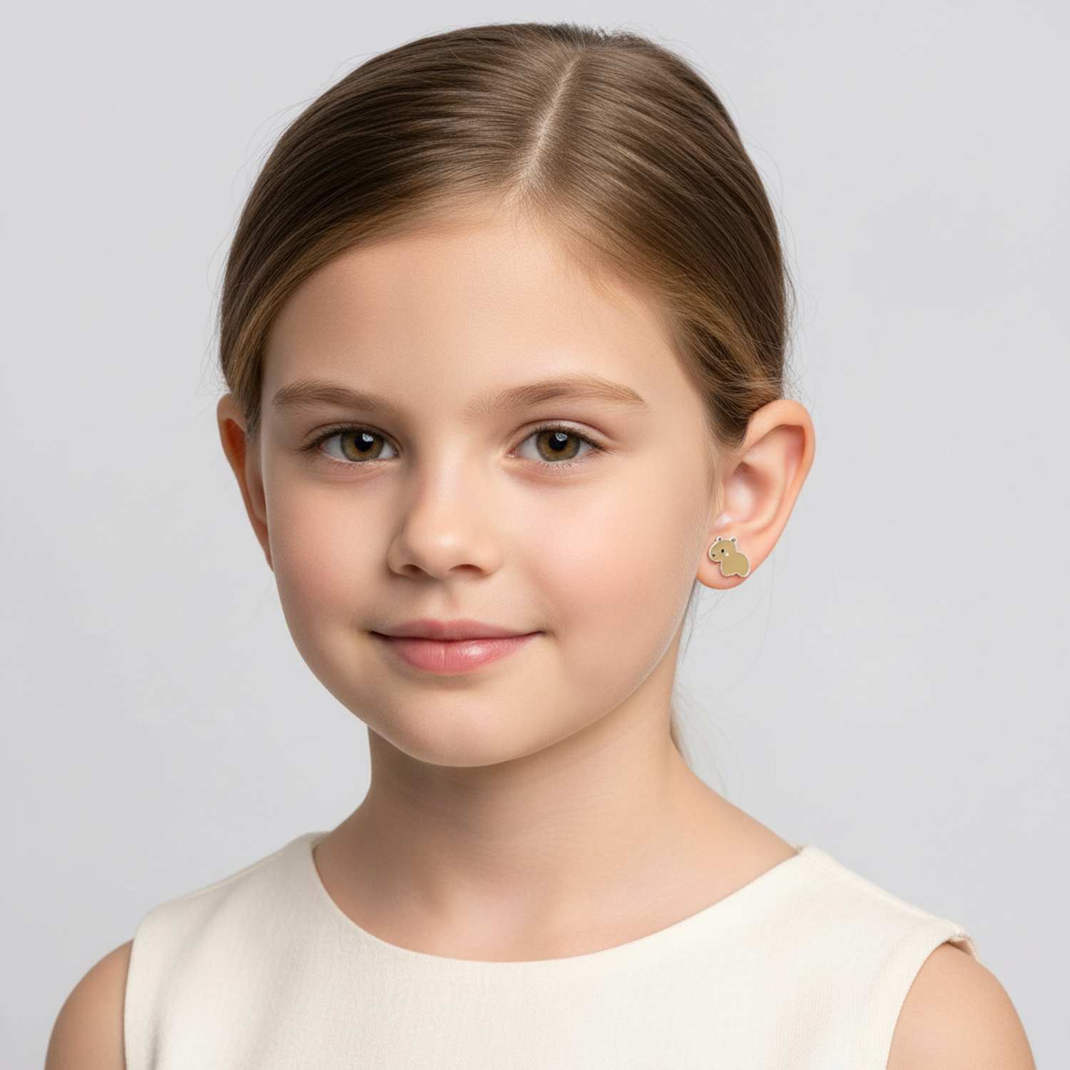 Young girl wearing gold capybara earrings for girls from Melchior Jewellery with subtle green enamel detail