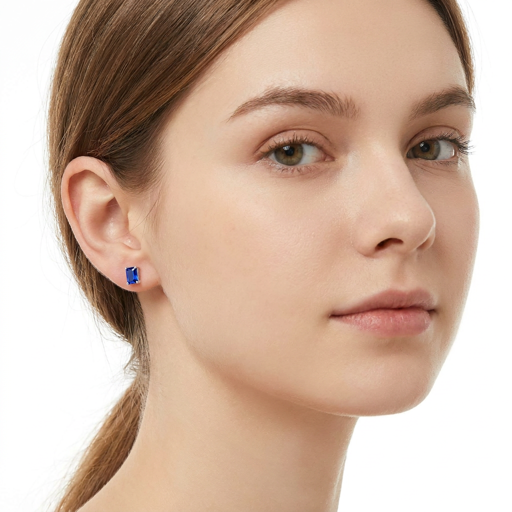 A close-up of a woman wearing a small rectangular blue stud earring with a gold setting against a clean white background.