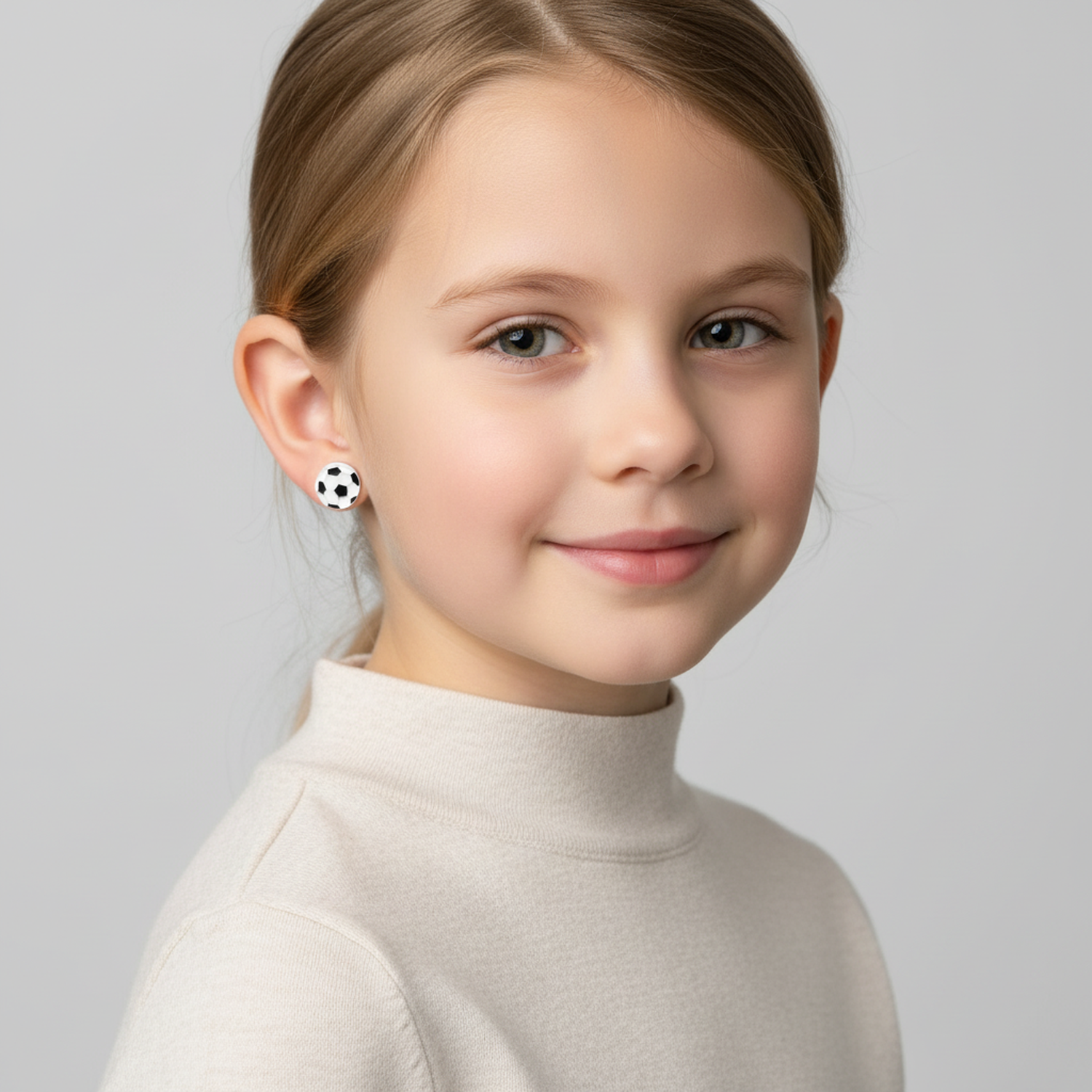 Child wearing football themed earrings for boys and girls by Melchior Jewellery with a happy expression