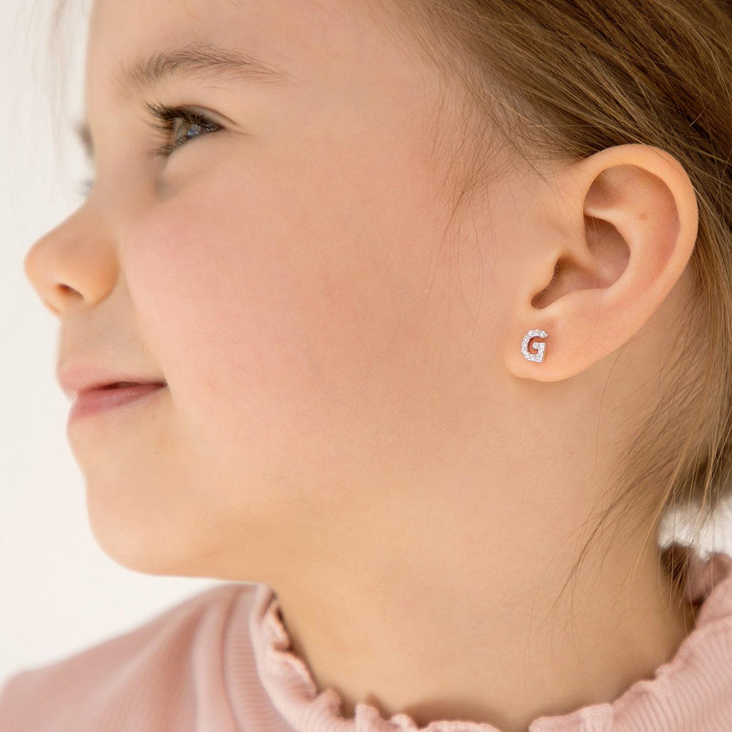 Girls sterling silver initial g earrings with sparkling clear stones worn by young girl with light brown hair and pink top