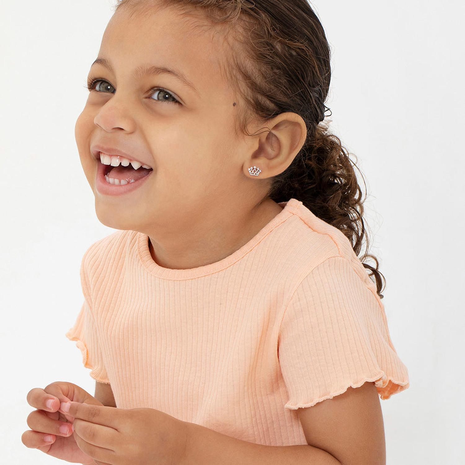 Smiling young girl wearing silver crown earrings girls from In Season Jewellery with peach top