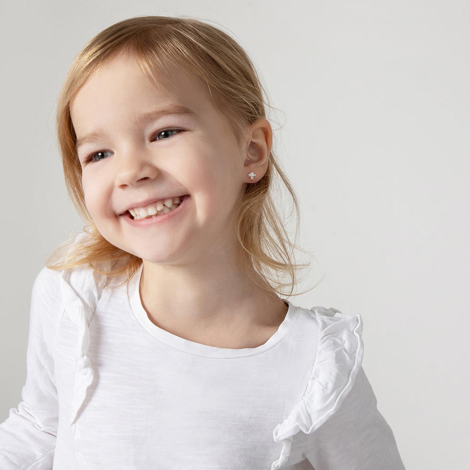 Young girl smiling wearing In Season Jewellery Girls CZ Cross Screw Back Earrings with clear sparkling stones and silver setting