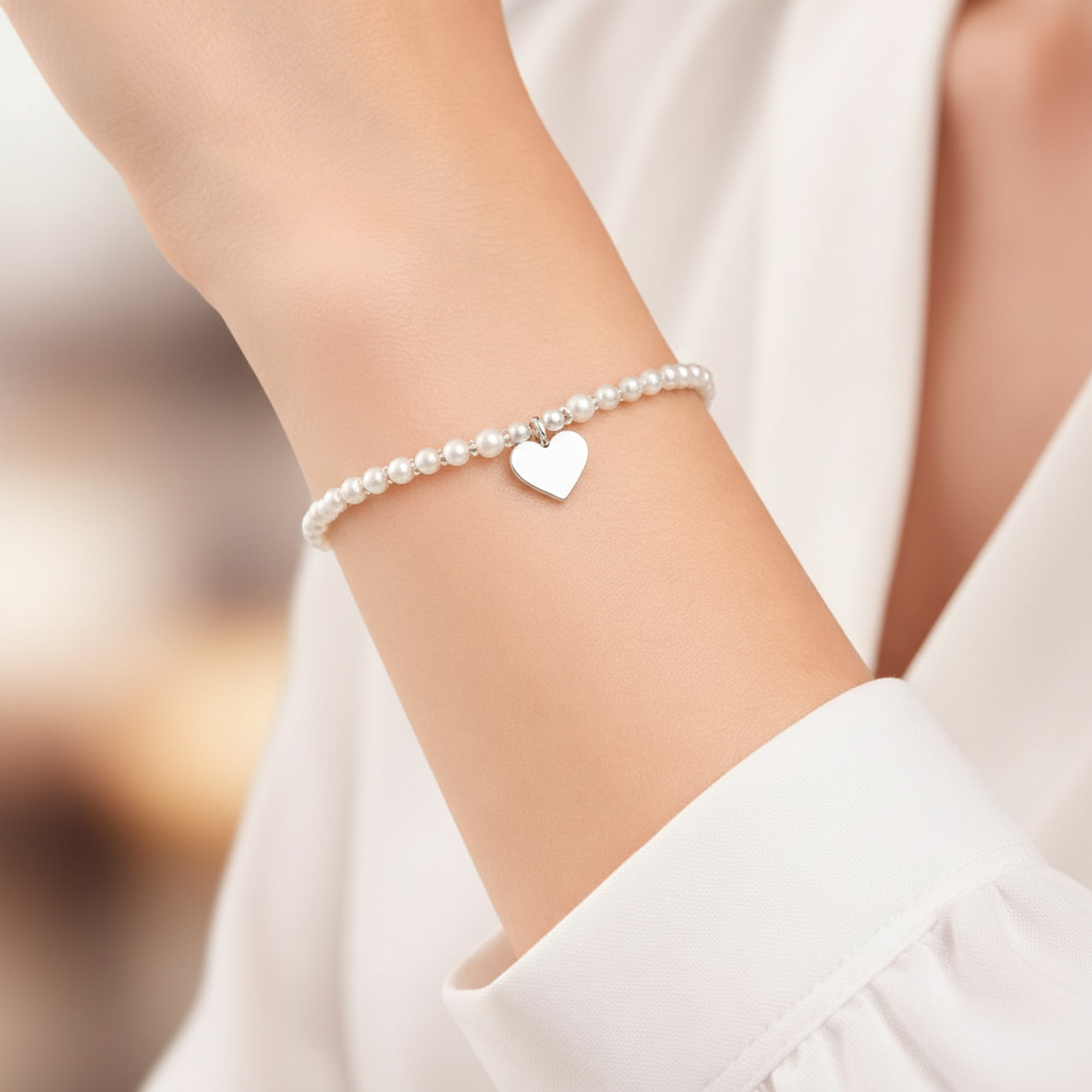 Freshwater pearl heart charm bracelet by Melchior Jewellery on womans wrist with white blouse