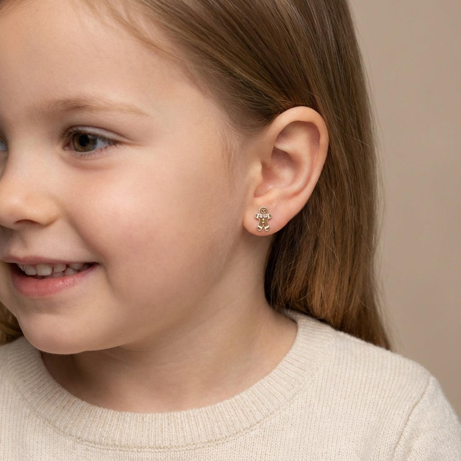 Child wearing Melchior Jewellery gingerbread man stud earrings with a smiling face and beige sweater