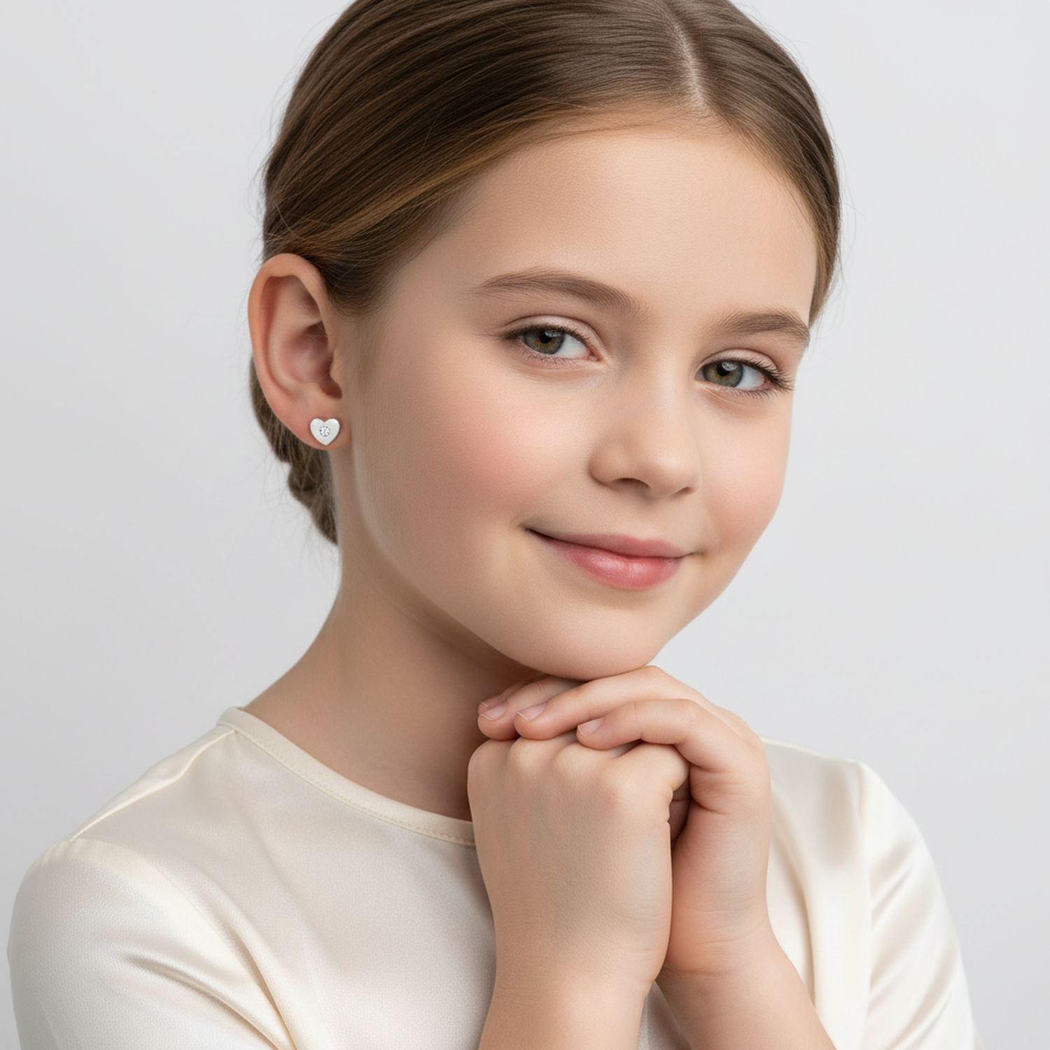 Young girl wearing heart shaped earrings for girls from Melchior Jewellery with a soft smile