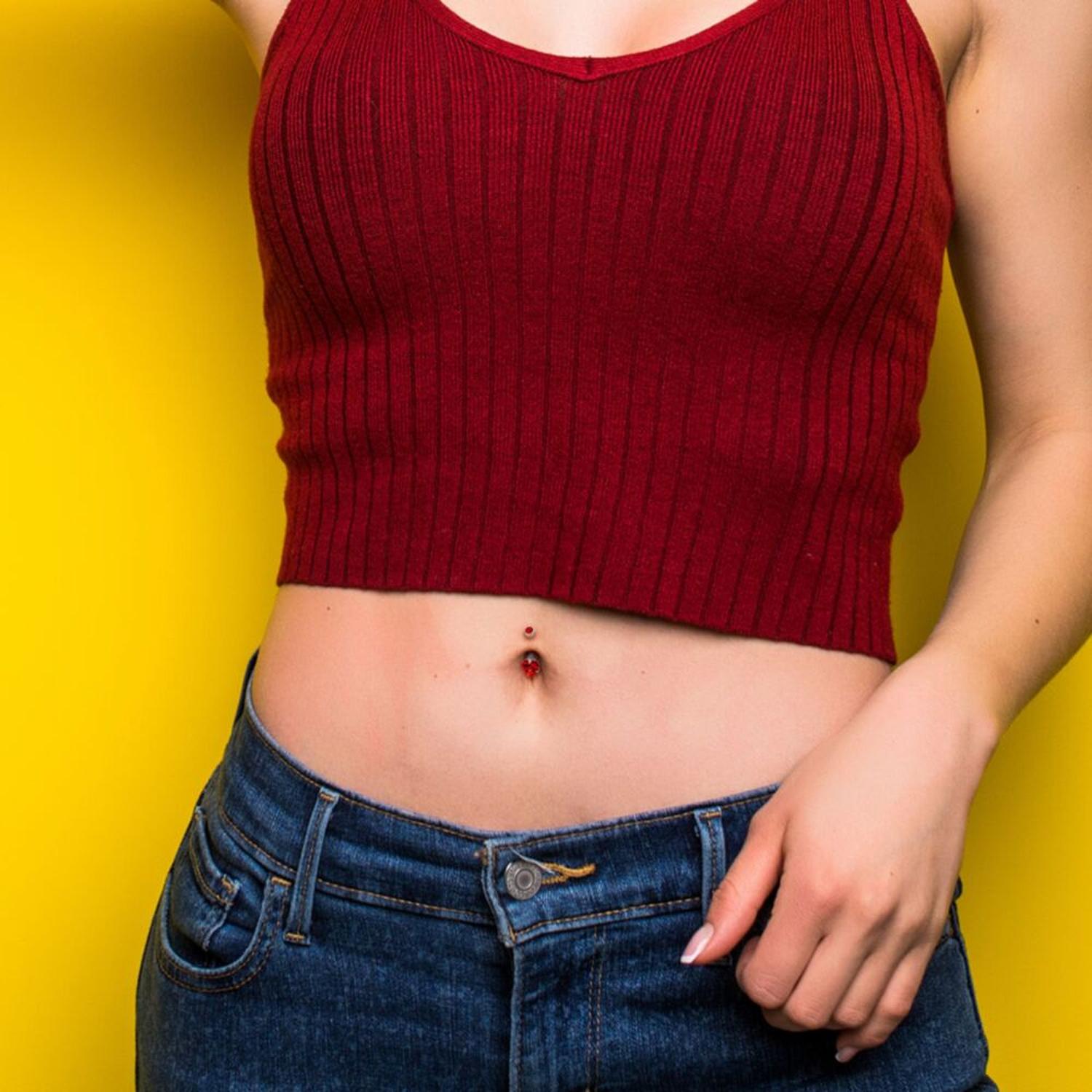 Melchior Jewellery titanium heart belly button bar worn on model midriff with red crop top and jeans