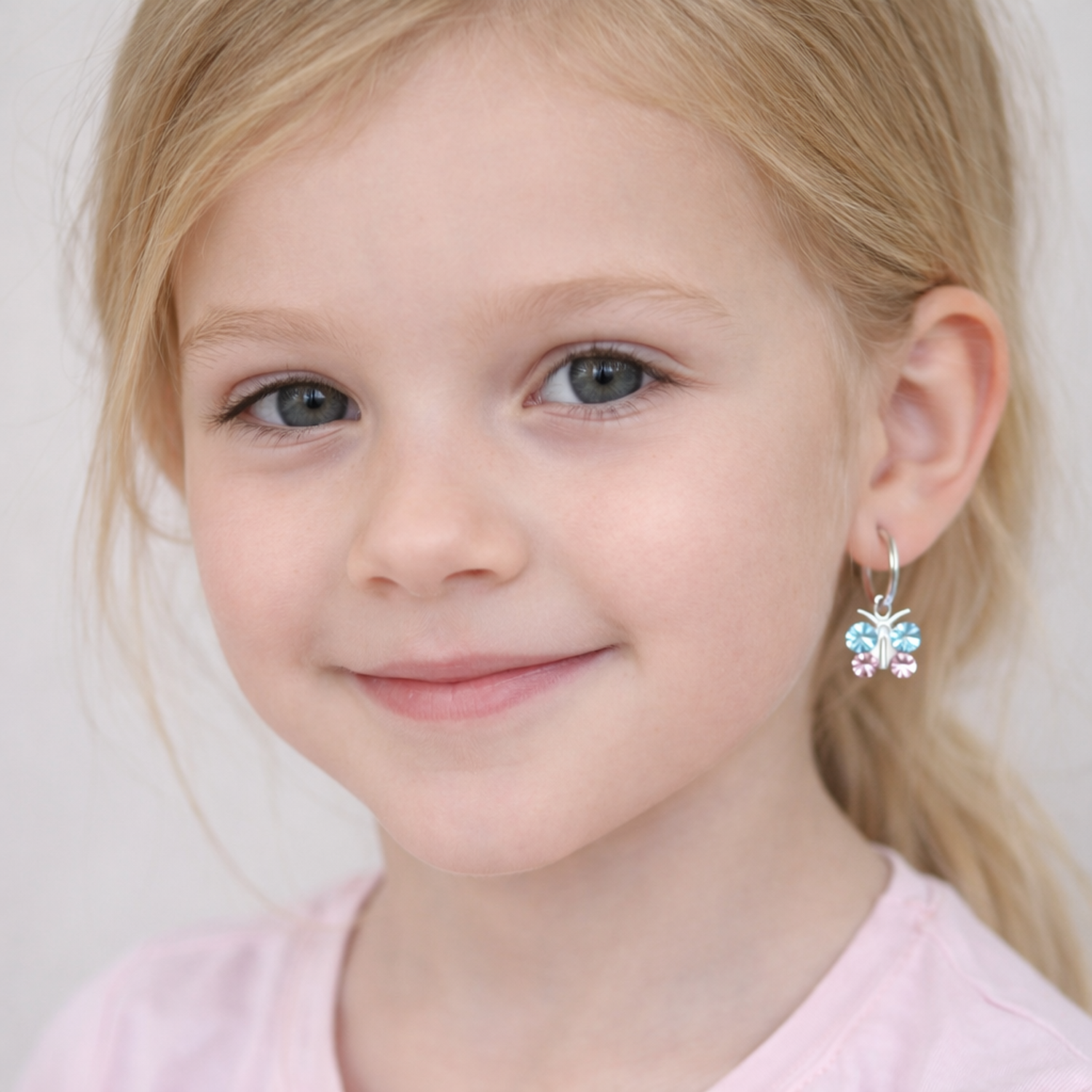Young girl wearing kids crystal butterfly hoop earrings by Melchior Jewellery smiling softly