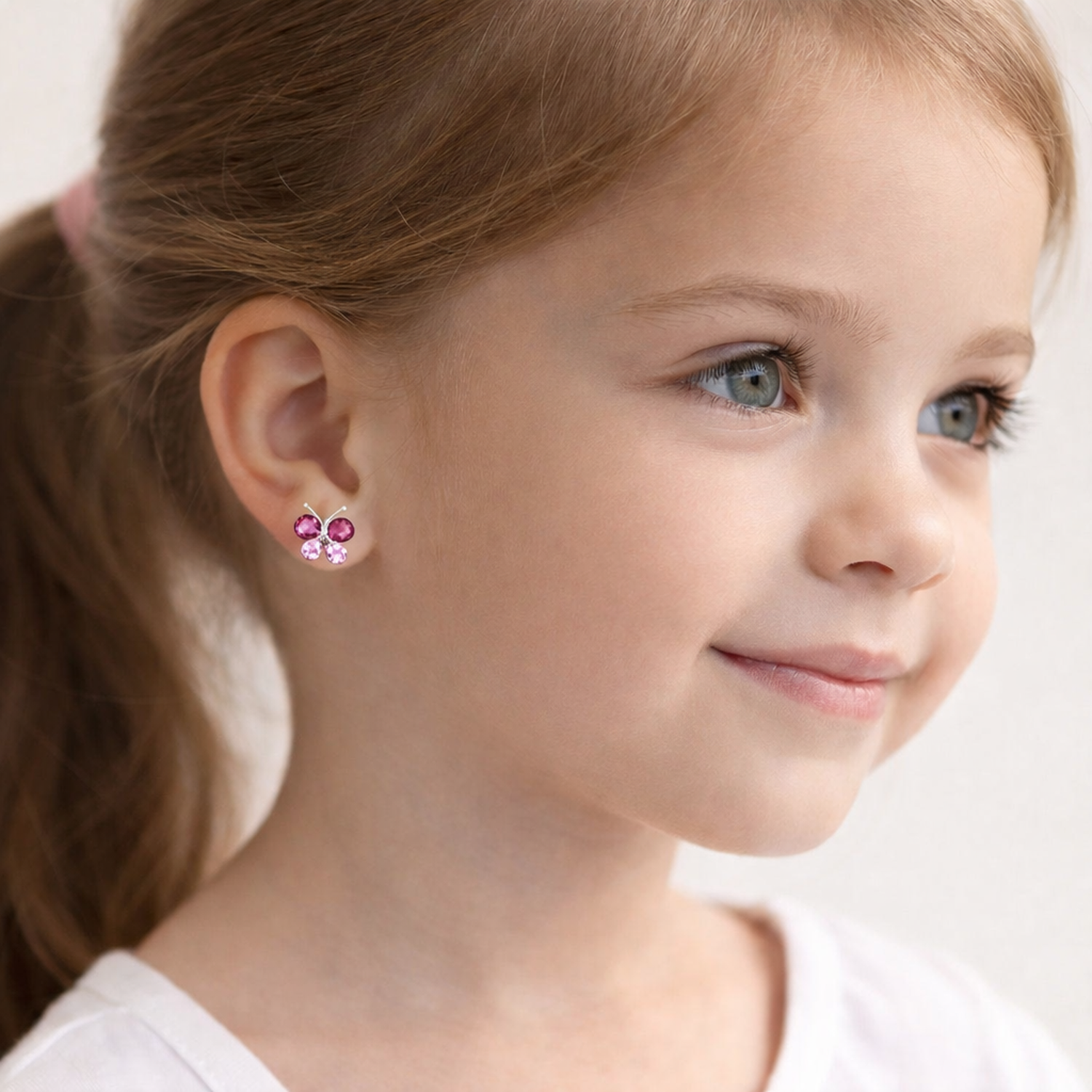 Young girl wearing pink butterfly stud earrings for kids from Melchior Jewellery with a smiling face