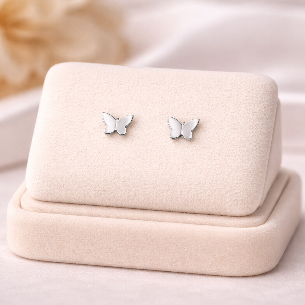 Delicate sterling silver butterfly earrings by Melchior Jewellery displayed on a soft beige velvet stand