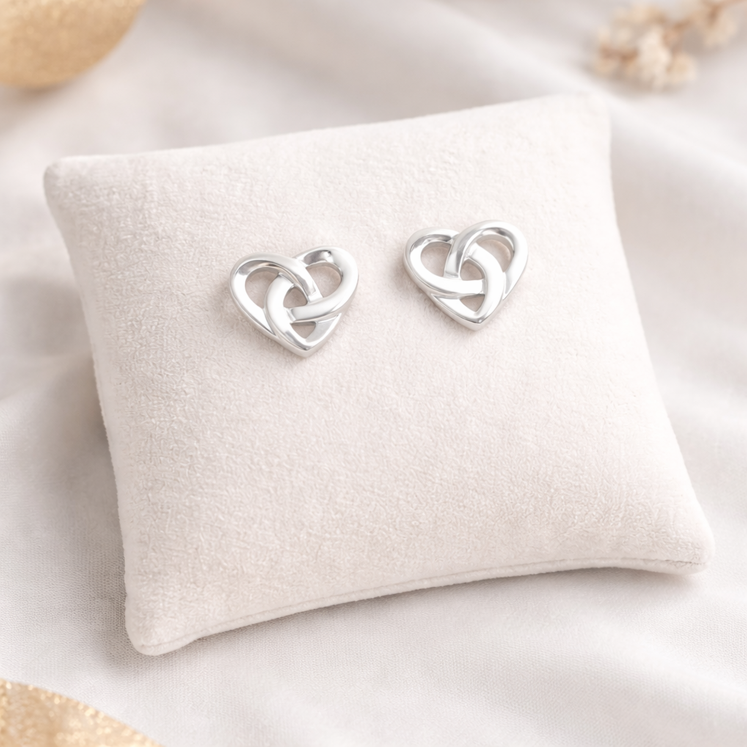 Sterling silver Celtic heart earrings displayed on soft beige cushion by Melchior Jewellery