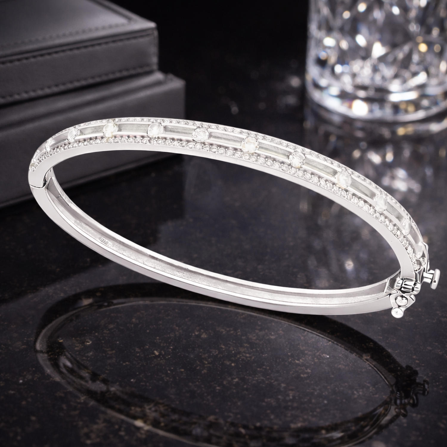 Sterling silver cubic zirconia bangle by Melchior Jewellery displayed on black surface with crystal glass background