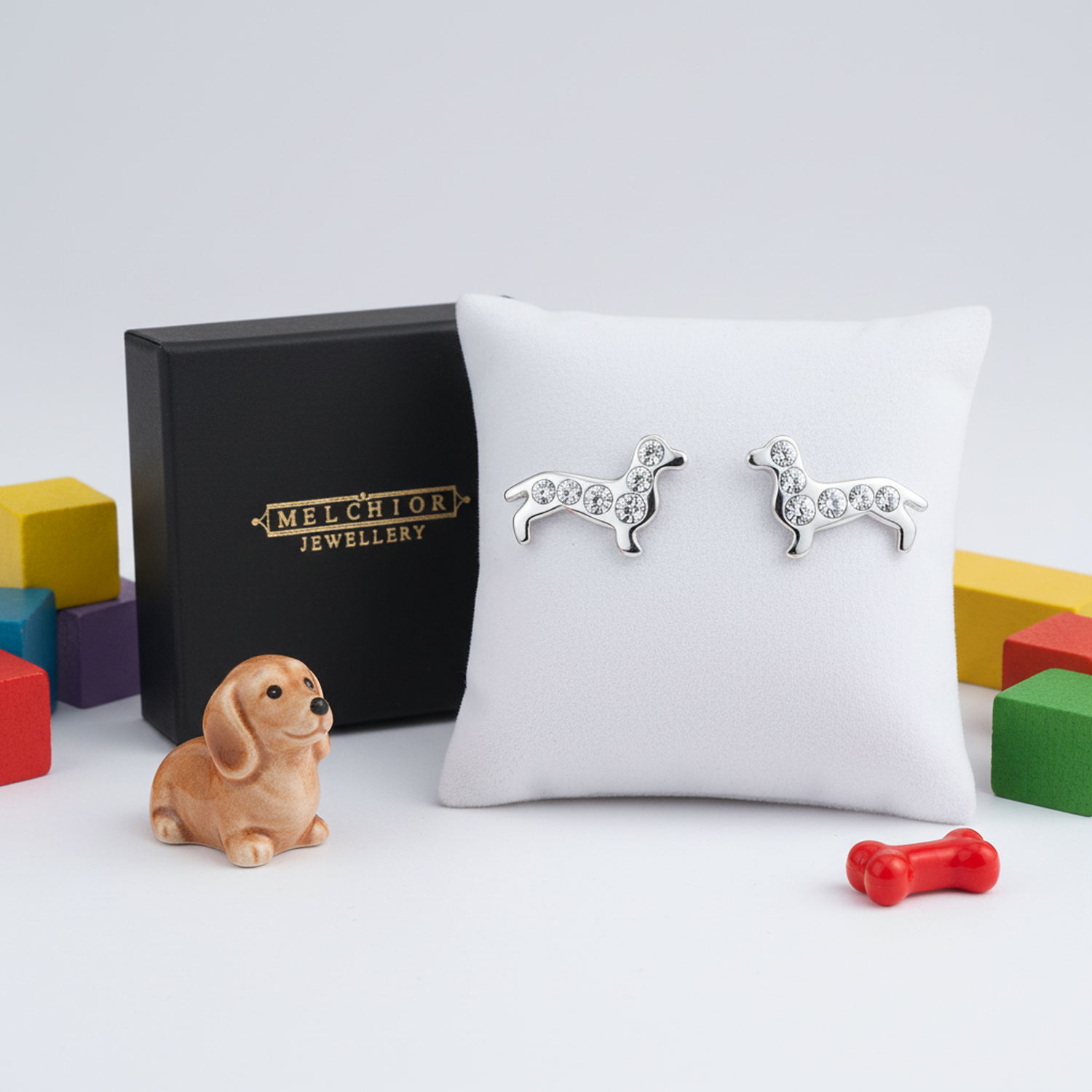 Sterling silver dachshund earrings with crystal details displayed on white cushion by Melchior Jewellery