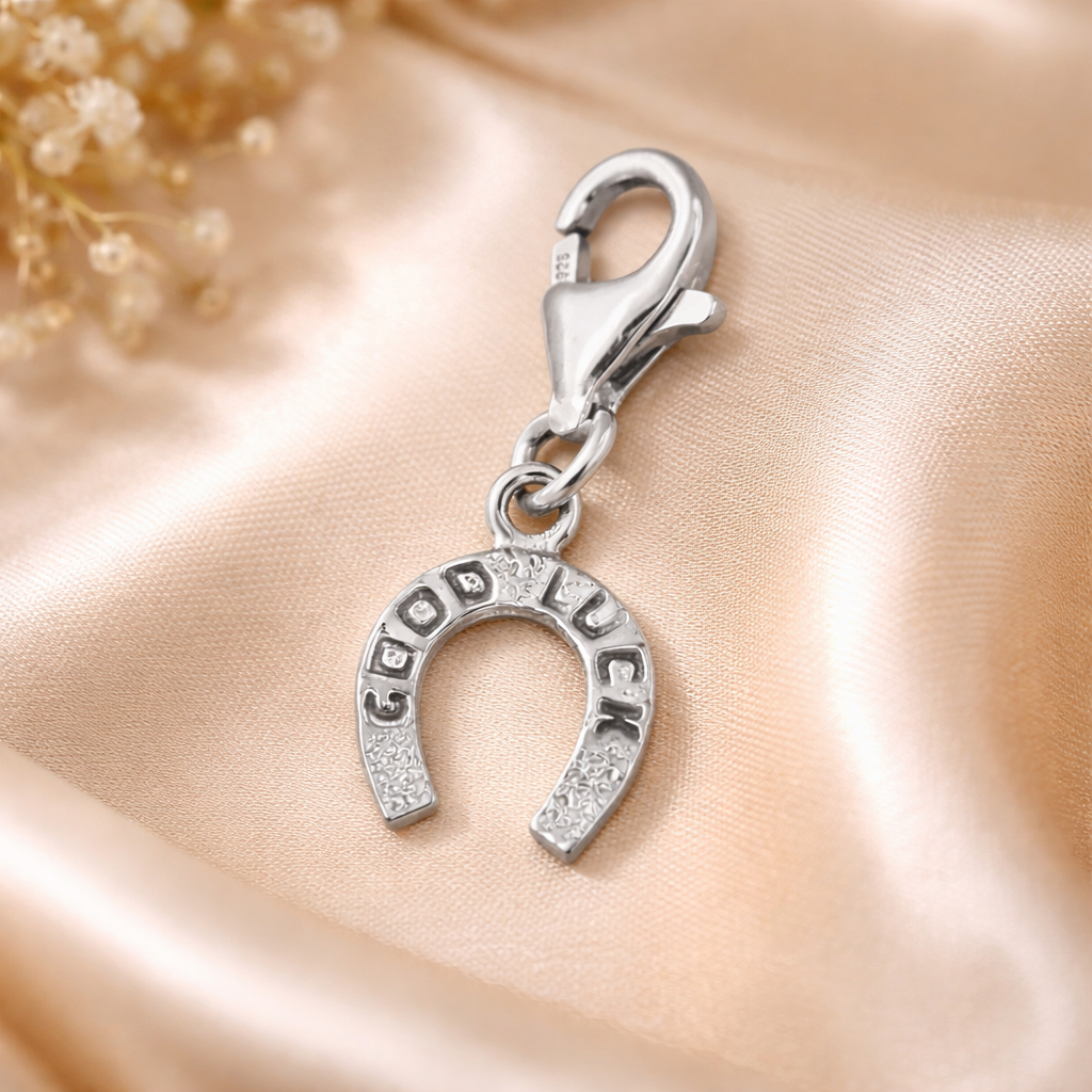 Sterling silver good luck charm horseshoe pendant with engraved 'Good Luck' text and lobster clasp on soft beige satin