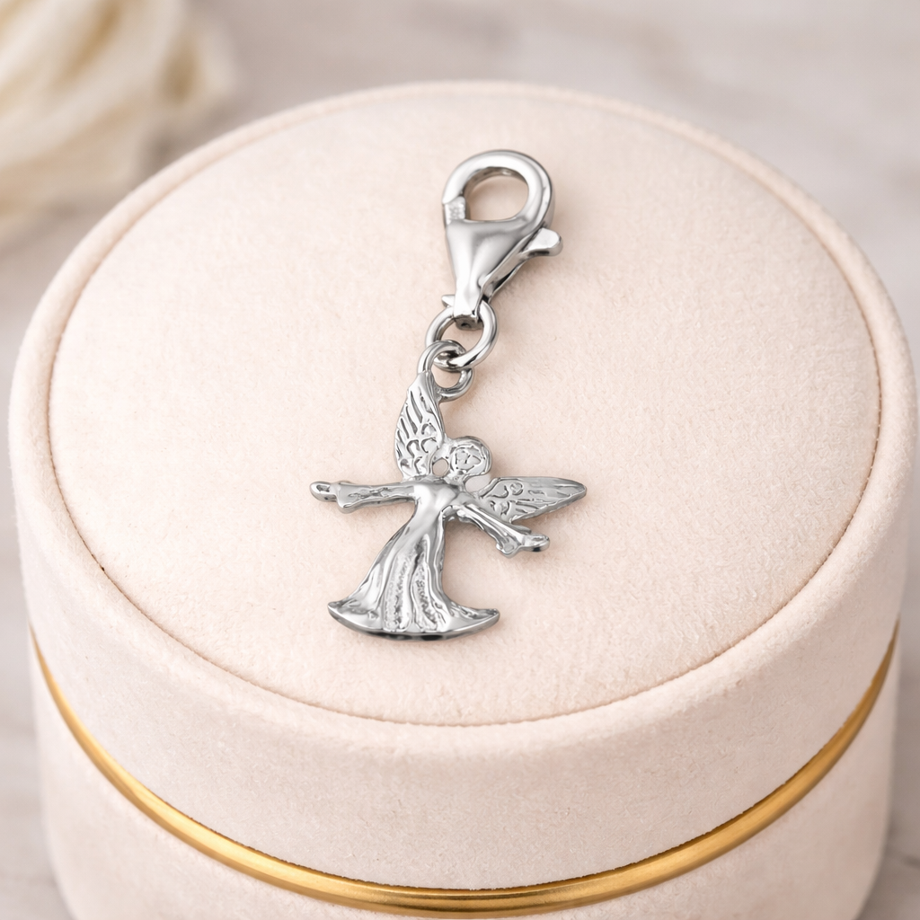Sterling silver guardian angel charm by Melchior Jewellery with detailed wings and flowing robe on a soft beige velvet box