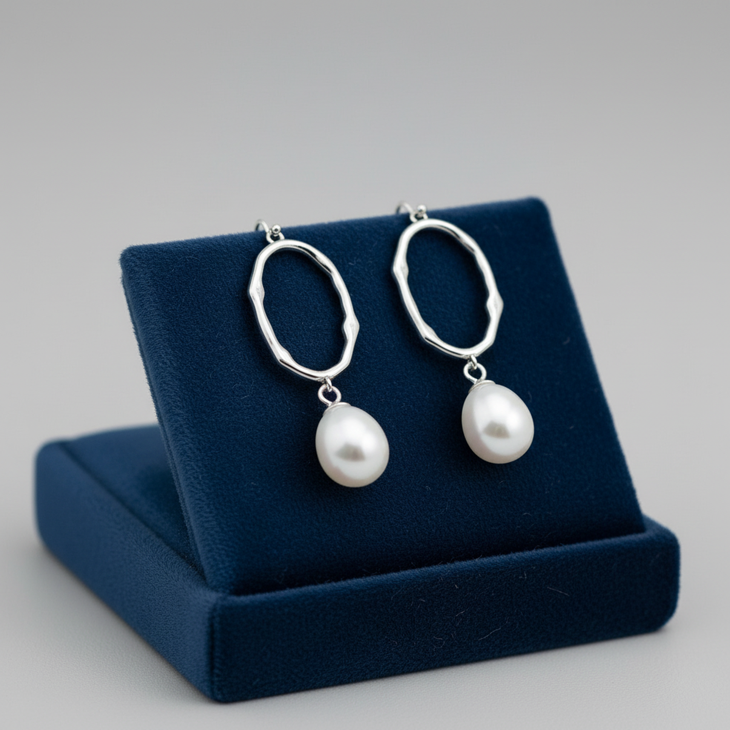 Sterling silver pearl drop earrings with oval textured hoops on navy blue display stand