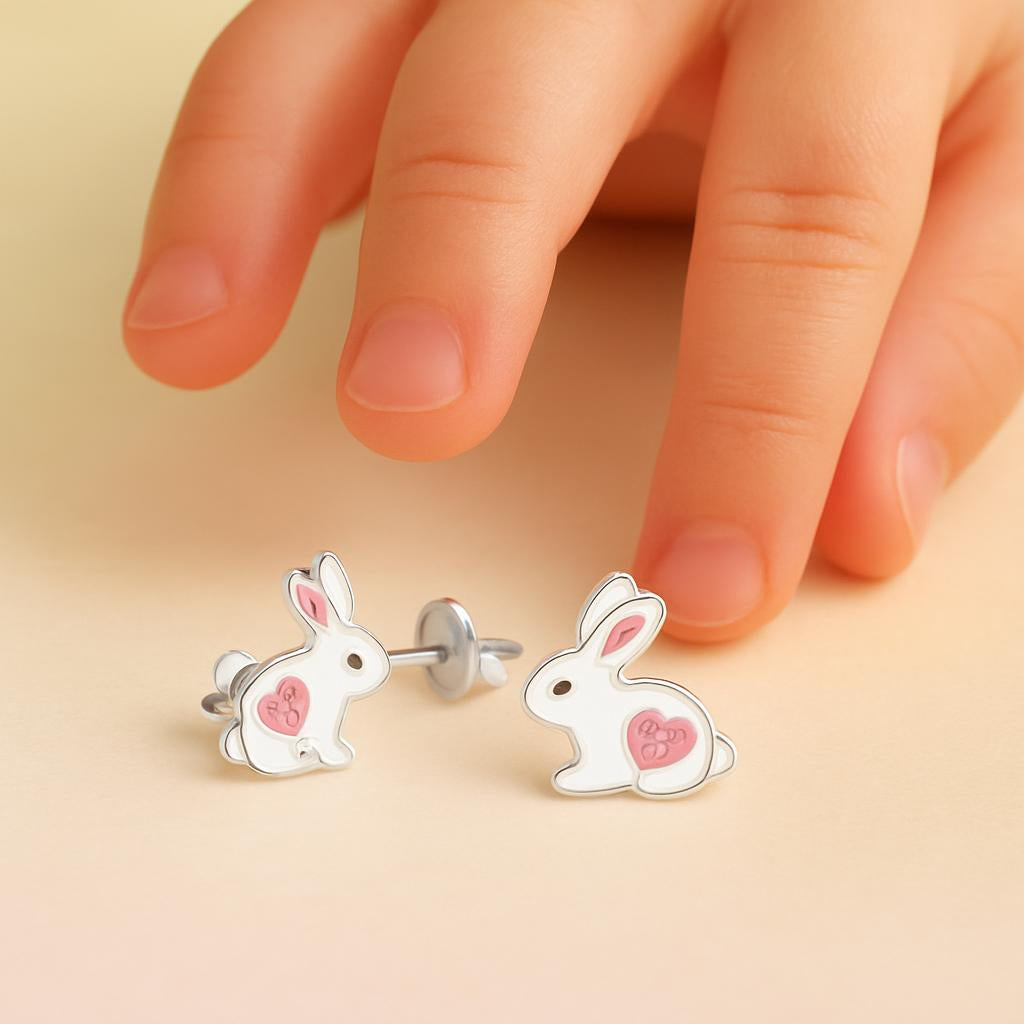 Sterling silver rabbit earrings for kids with pink heart details by Melchior Jewellery next to a child's fingers