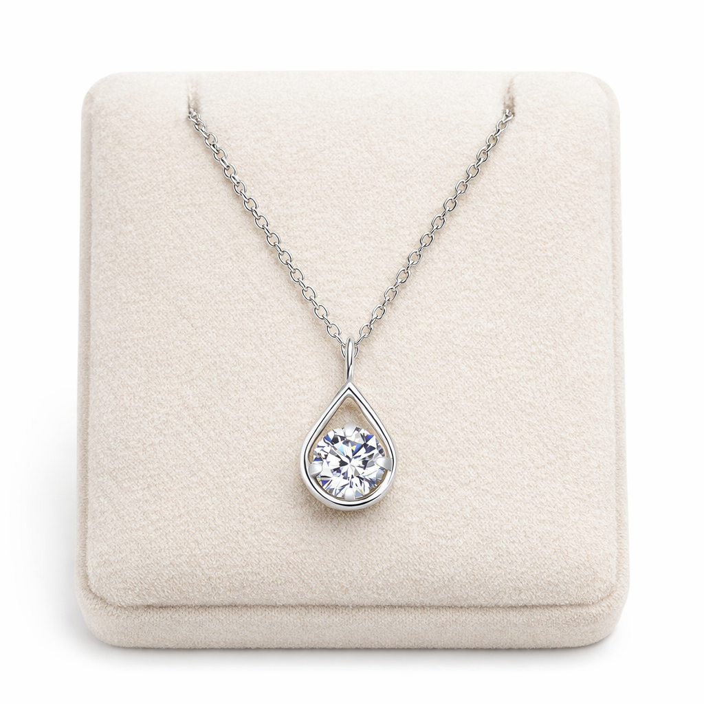 Sterling silver teardrop pendant necklace with sparkling gemstone displayed on cream cushion